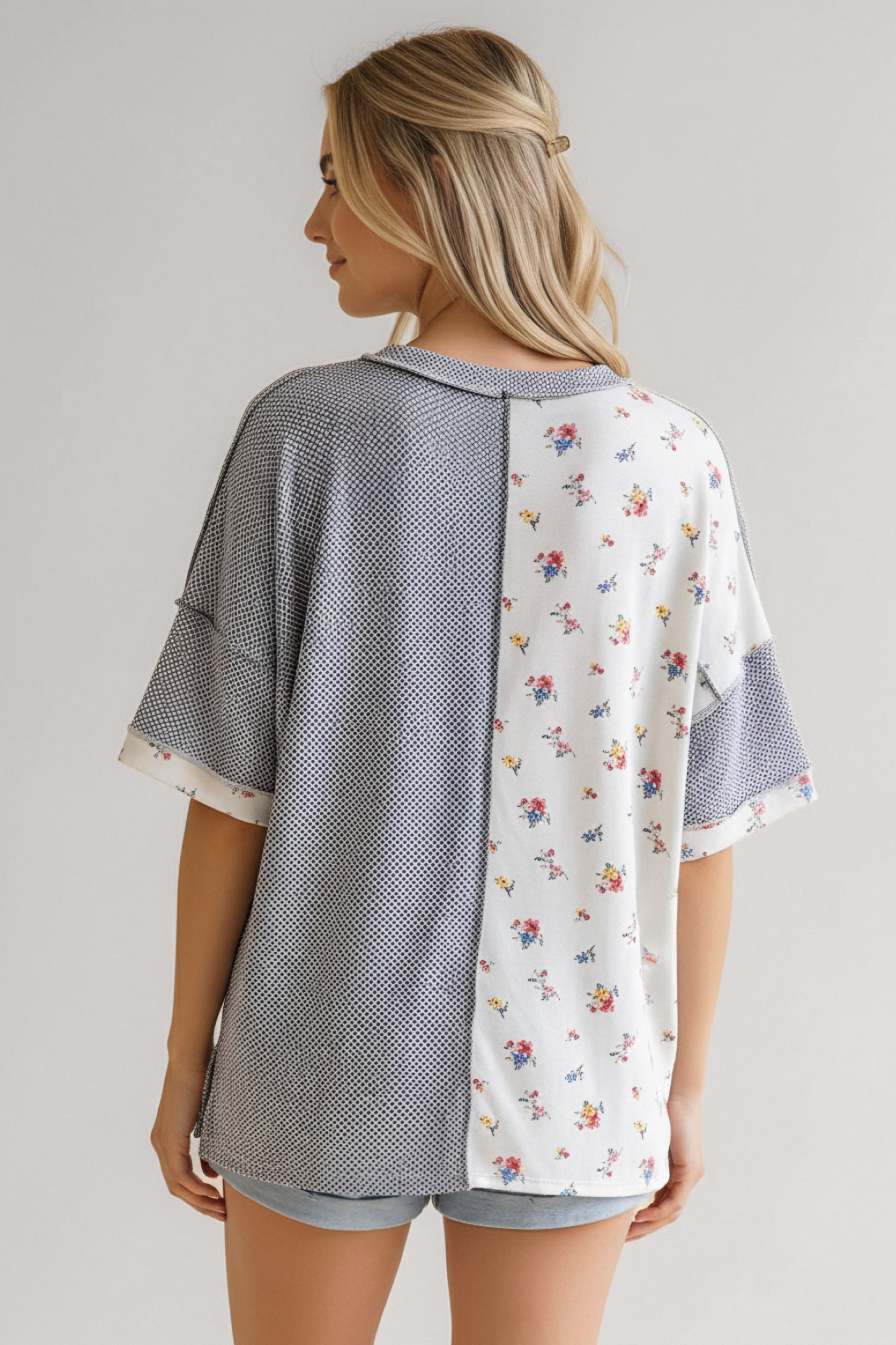 Woman wearing a loose blue and white top with small floral print and textured knit panels paired with light denim shorts