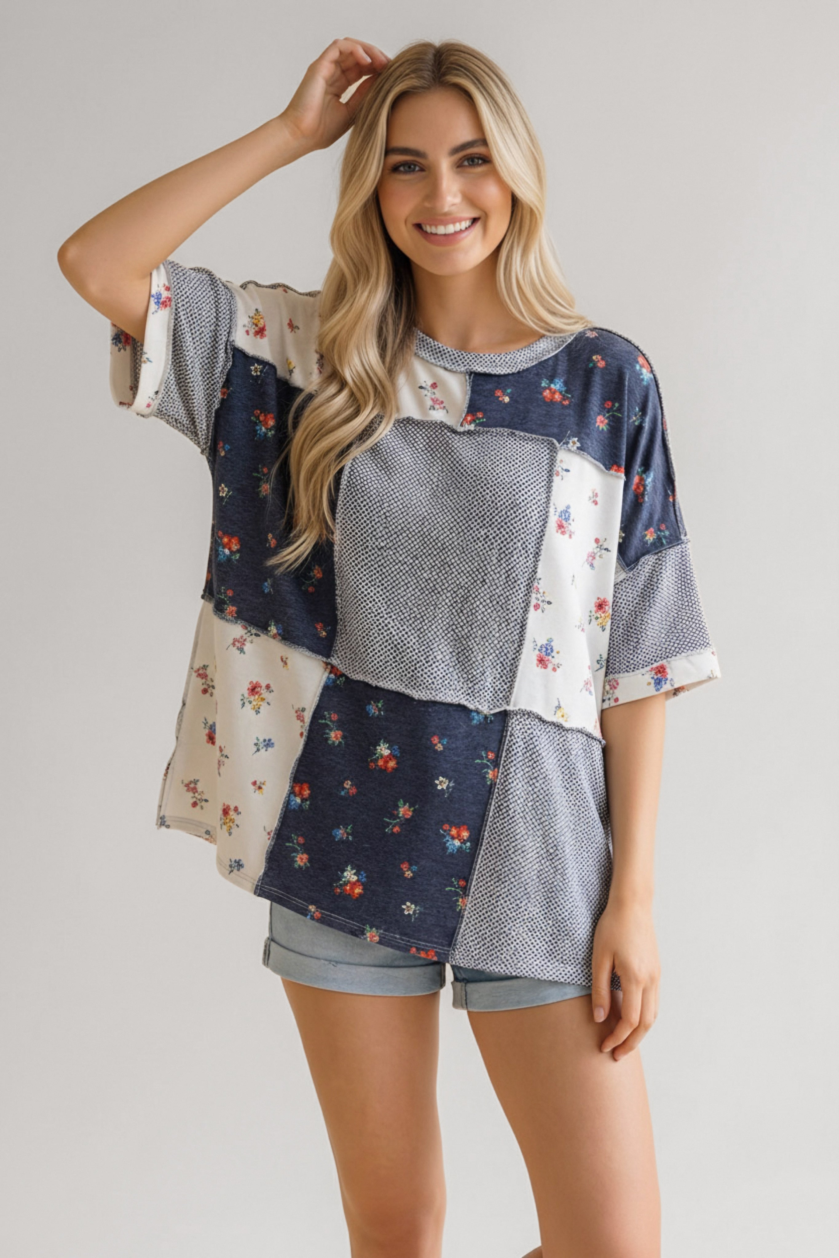 Woman wearing a loose patchwork top with navy blue and cream floral and geometric patterns paired with light denim shorts