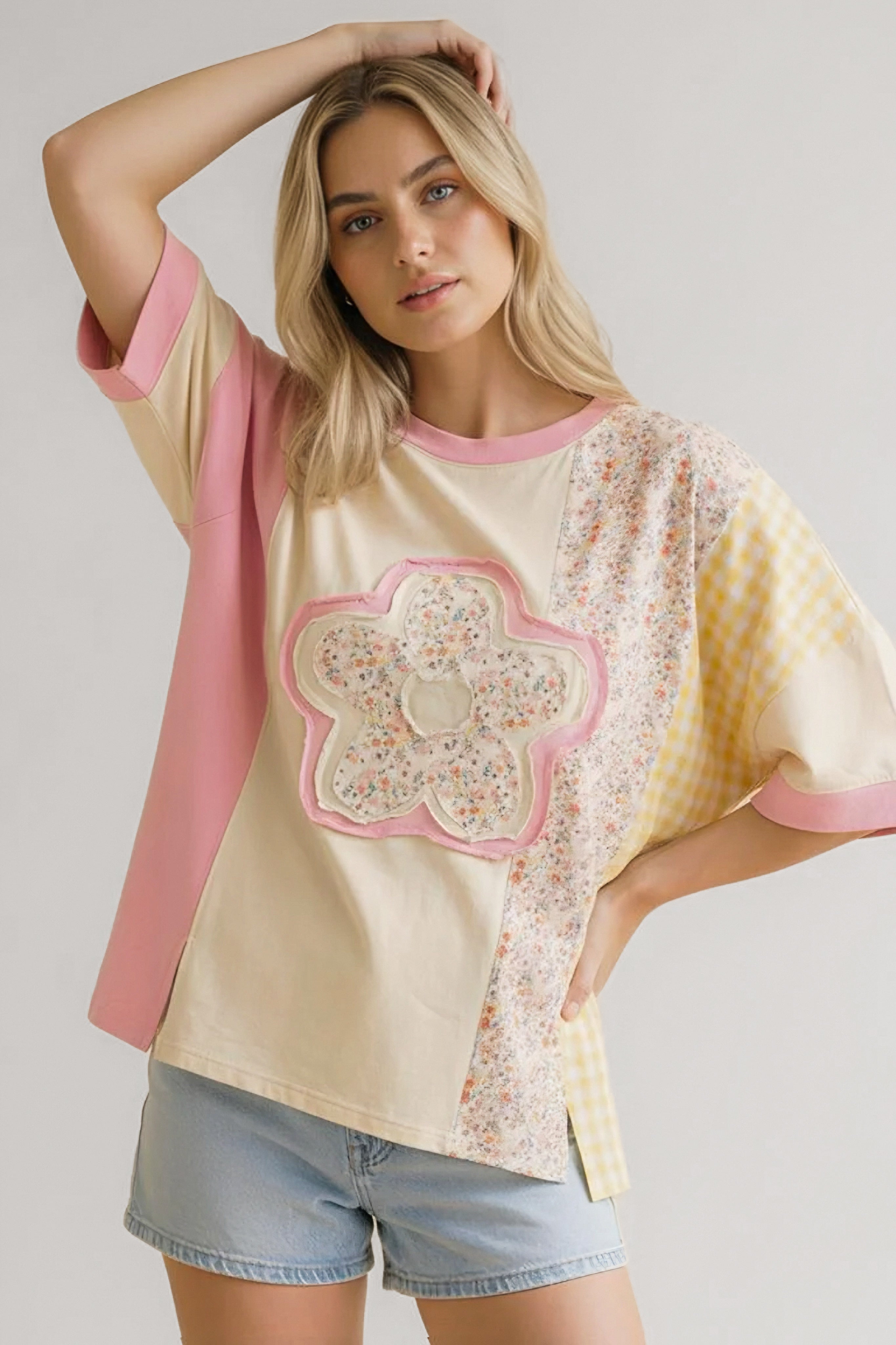 Woman wearing relaxed patchwork tee with floral applique and pastel pink, cream, and yellow panels paired with denim shorts