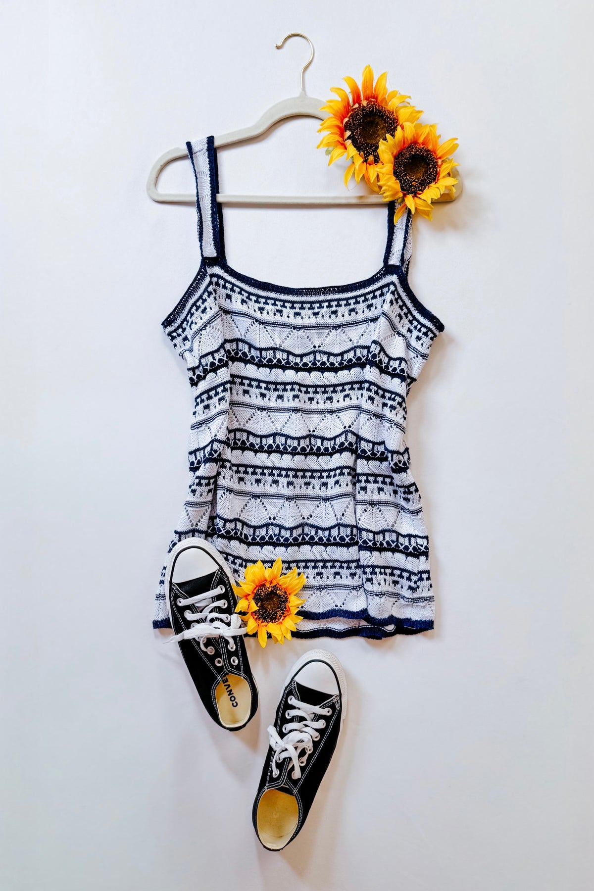 Blue and white pointelle sweater tank with scalloped trim styled on a hanger with black sneakers and sunflower accents