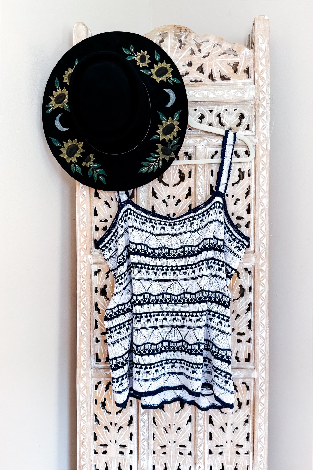 Blue and white pointelle sweater tank with scalloped trim and patterned knit stripes hanging beneath a floral embroidered black hat