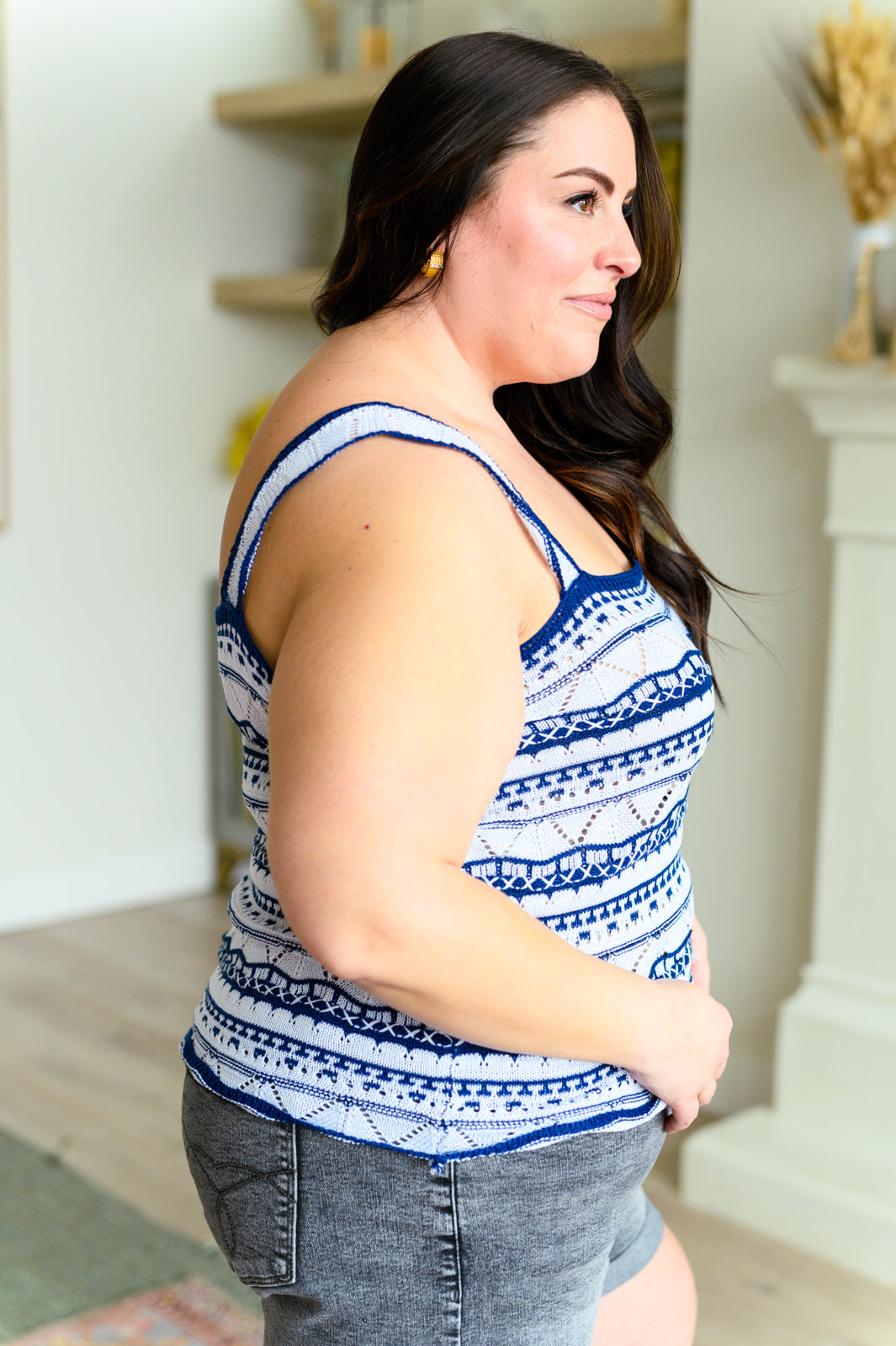 Side view of woman wearing blue patterned sweater tank with thin straps and gray denim shorts indoors