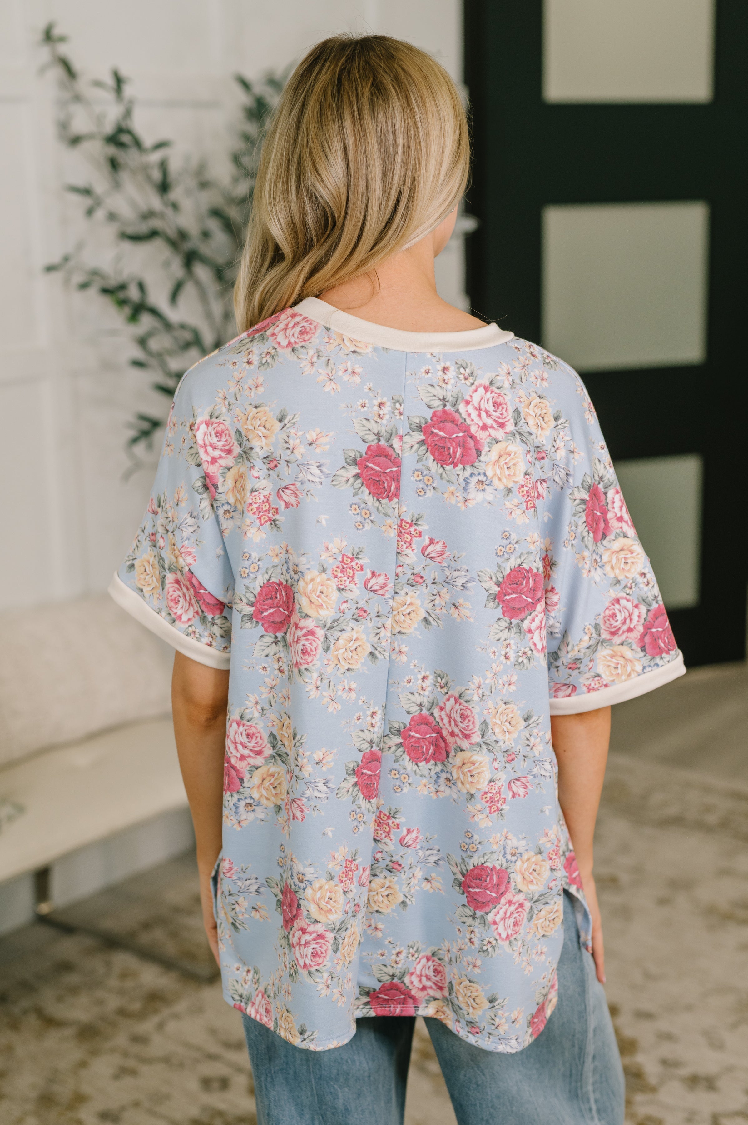 Back view of relaxed blue floral print tee with cream trim worn by woman in casual indoor setting