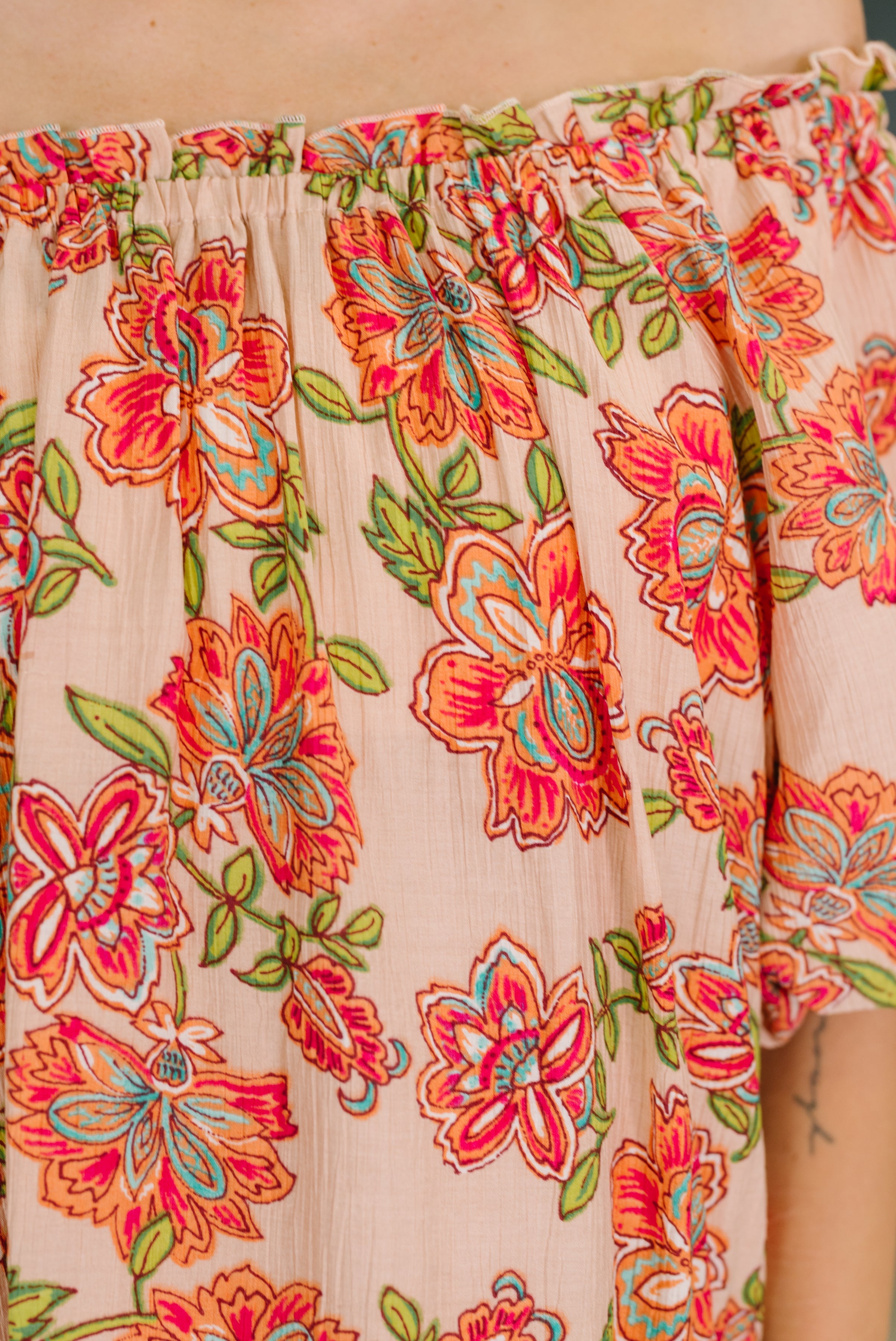 Close-up of floral patterned orange off-shoulder blouse featuring vibrant flower and leaf details on soft fabric