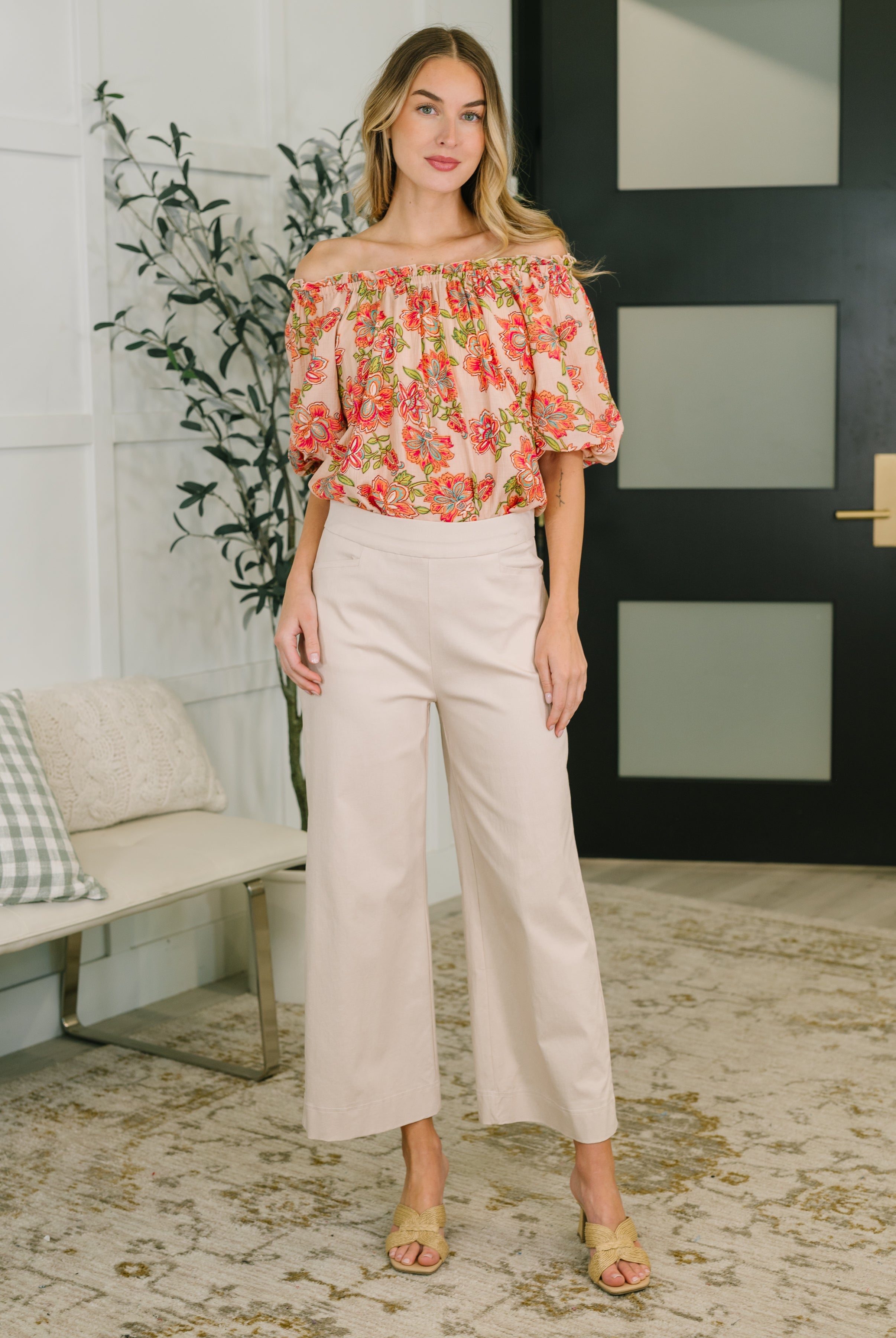 Woman wearing orange floral off-the-shoulder blouse with puff sleeves paired with beige wide-leg pants indoors