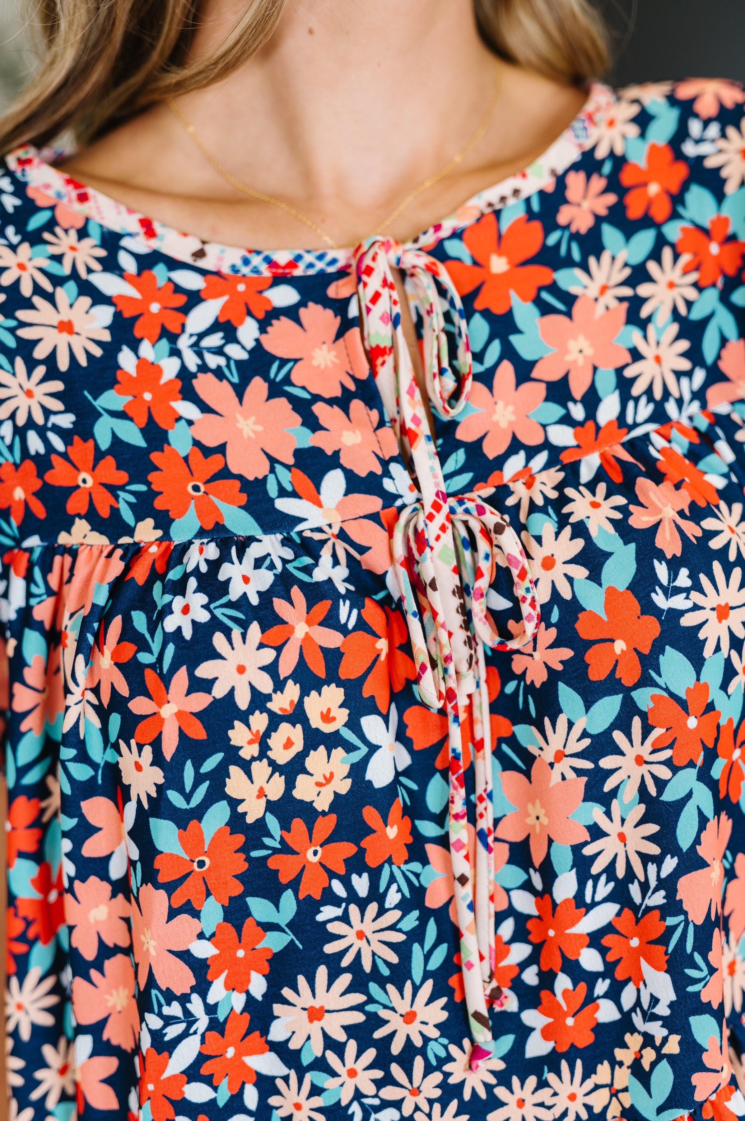 Close-up of navy woven dress fabric with bright floral print and delicate neck ties showcasing free-spirited charm
