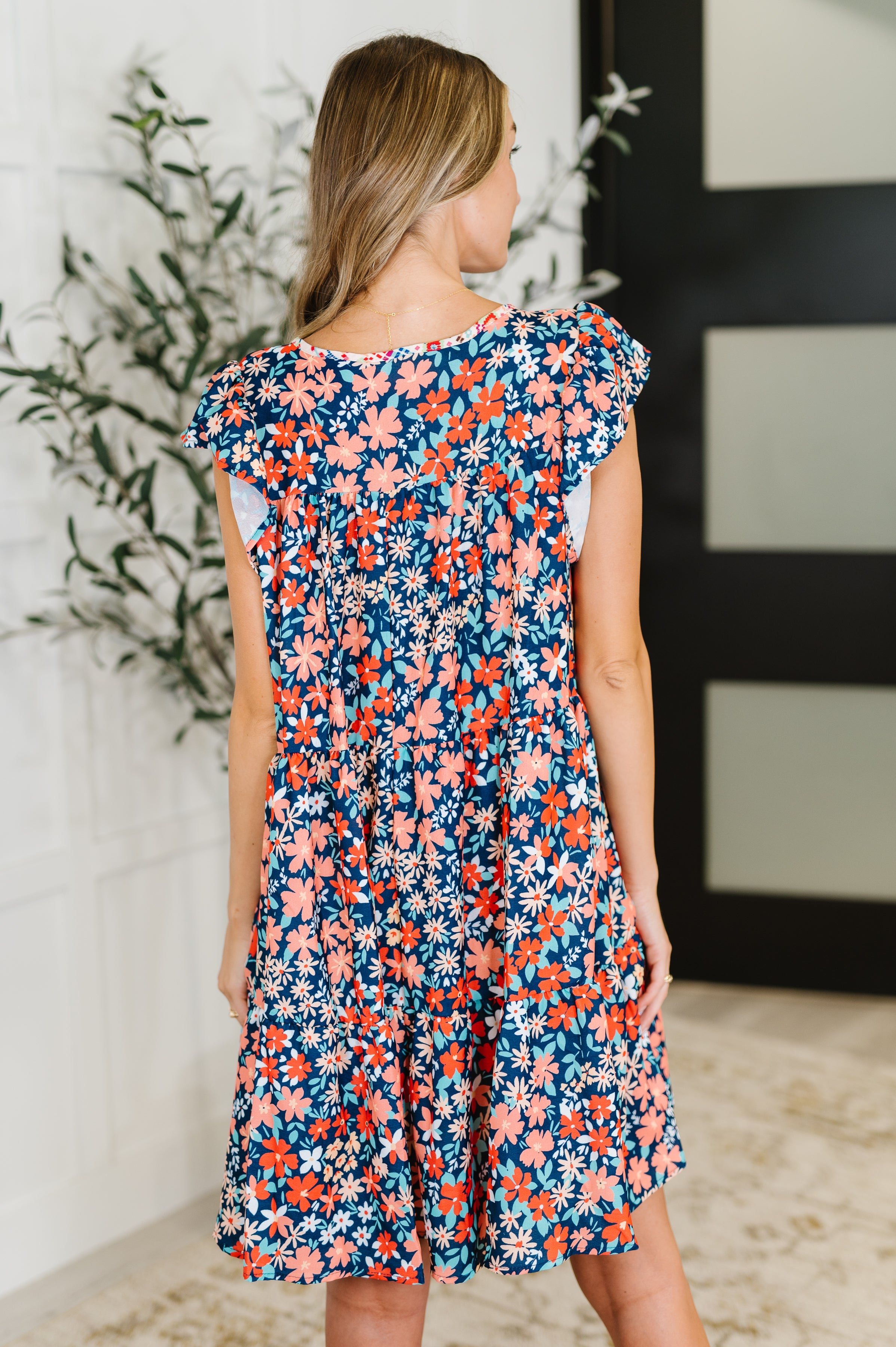 Back view of woman wearing a floral patterned dress with flutter sleeves in a bright indoor setting