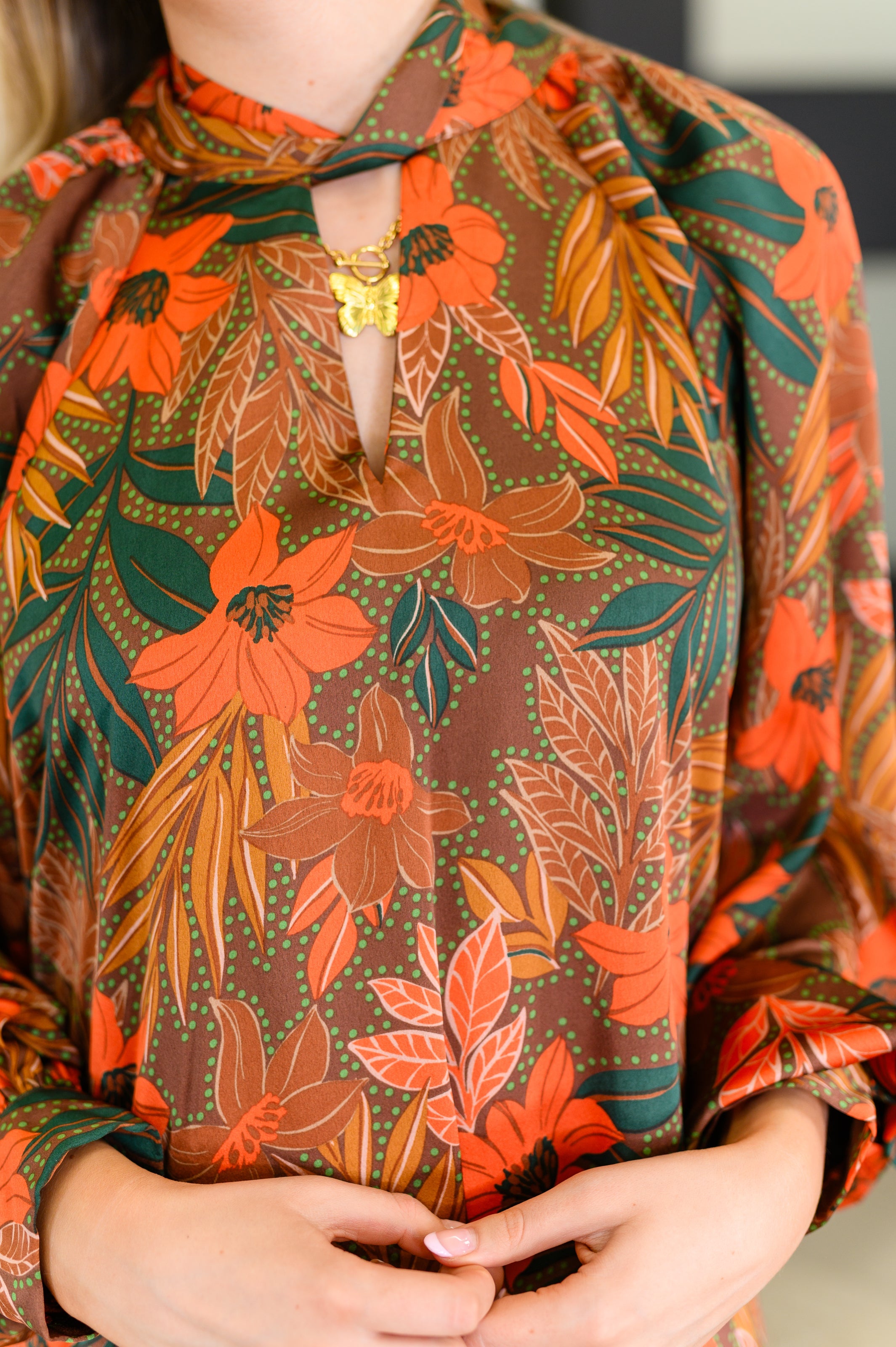 Close-up of rust floral balloon sleeve dress with keyhole neckline and butterfly pendant necklace worn indoors