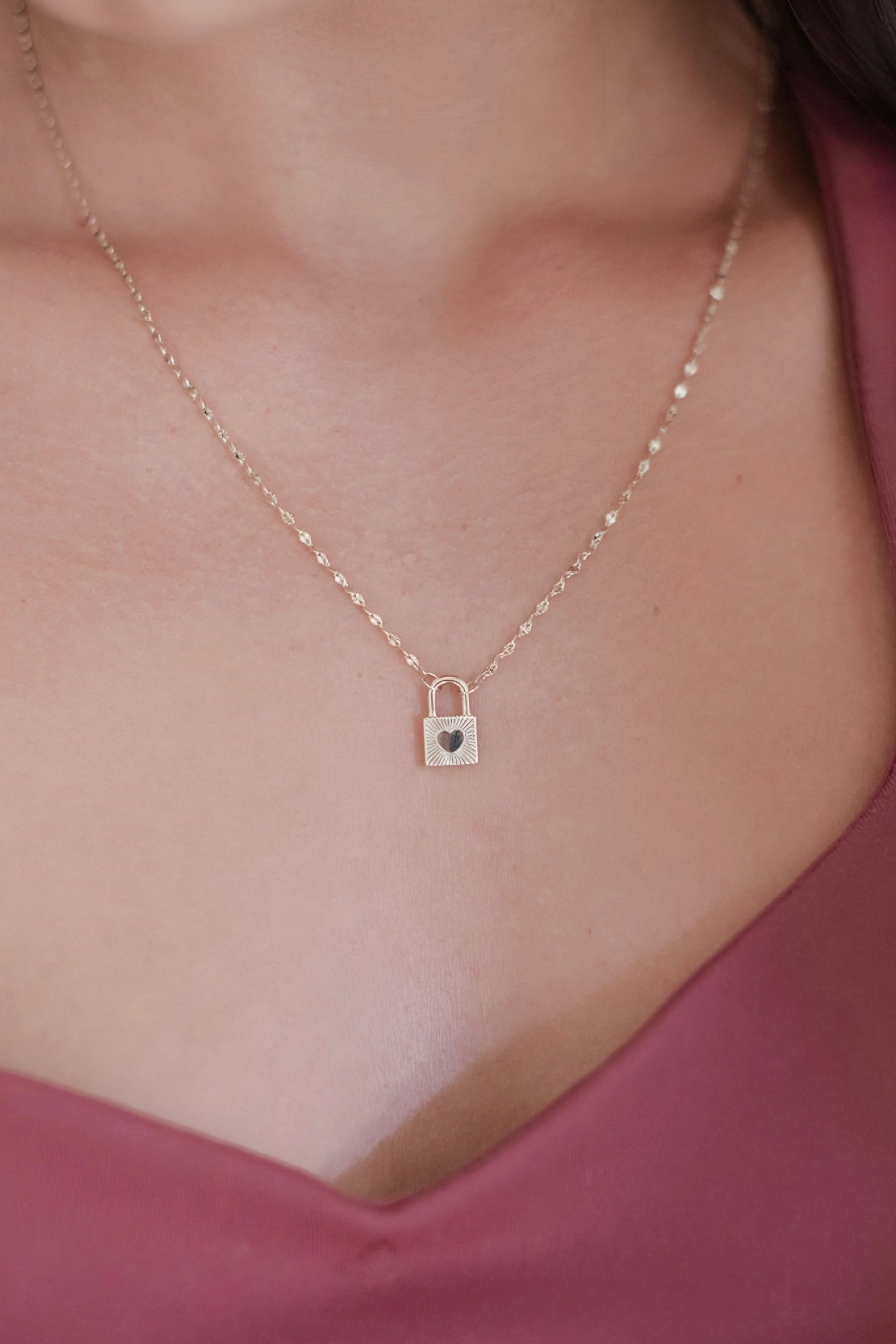 Close-up of gold love locked necklace with heart detail worn on delicate chain above mauve v-neck top