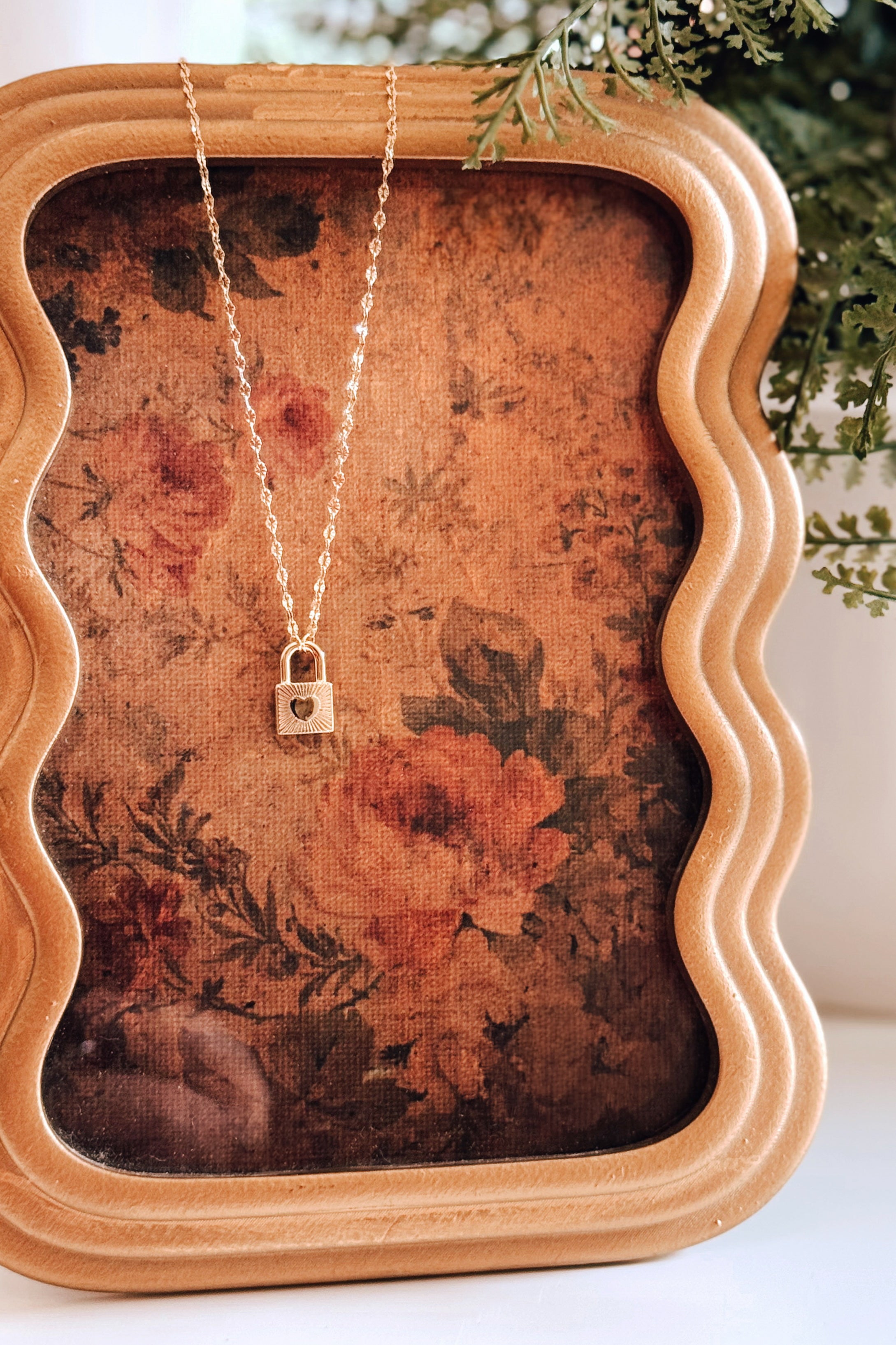Gold love locked pendant necklace with delicate chain displayed on vintage floral fabric in eclectic style