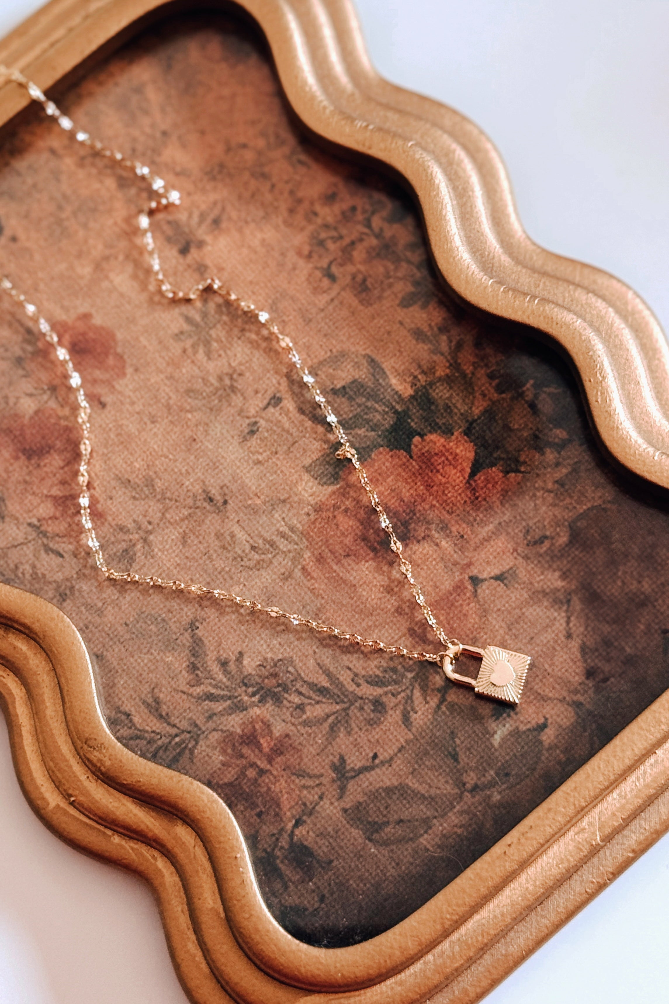 Gold love-locked necklace with delicate chain resting on vintage floral fabric in eclectic and free-spirited style