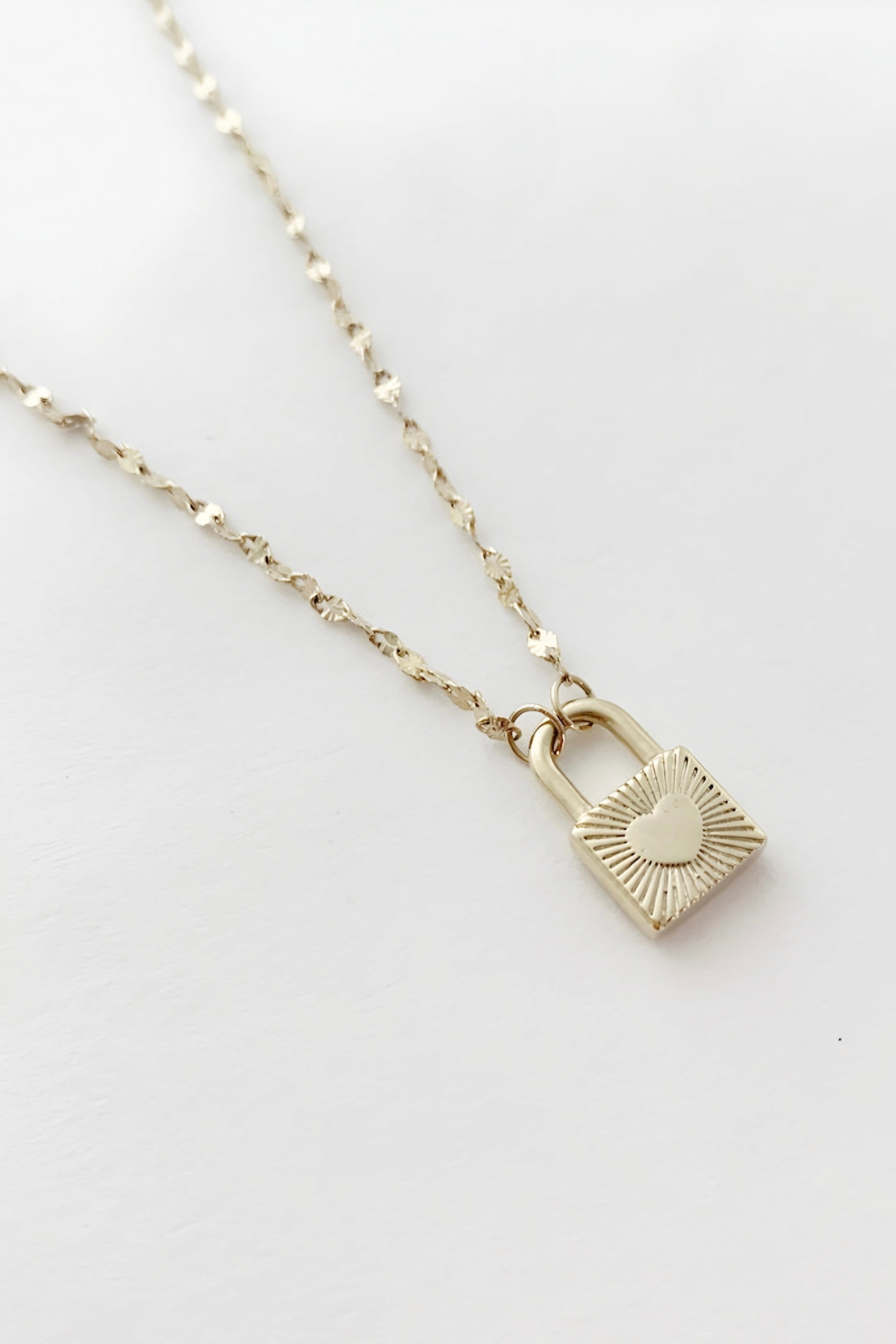 Gold padlock pendant with heart accent on textured chain against plain white backdrop in eclectic style