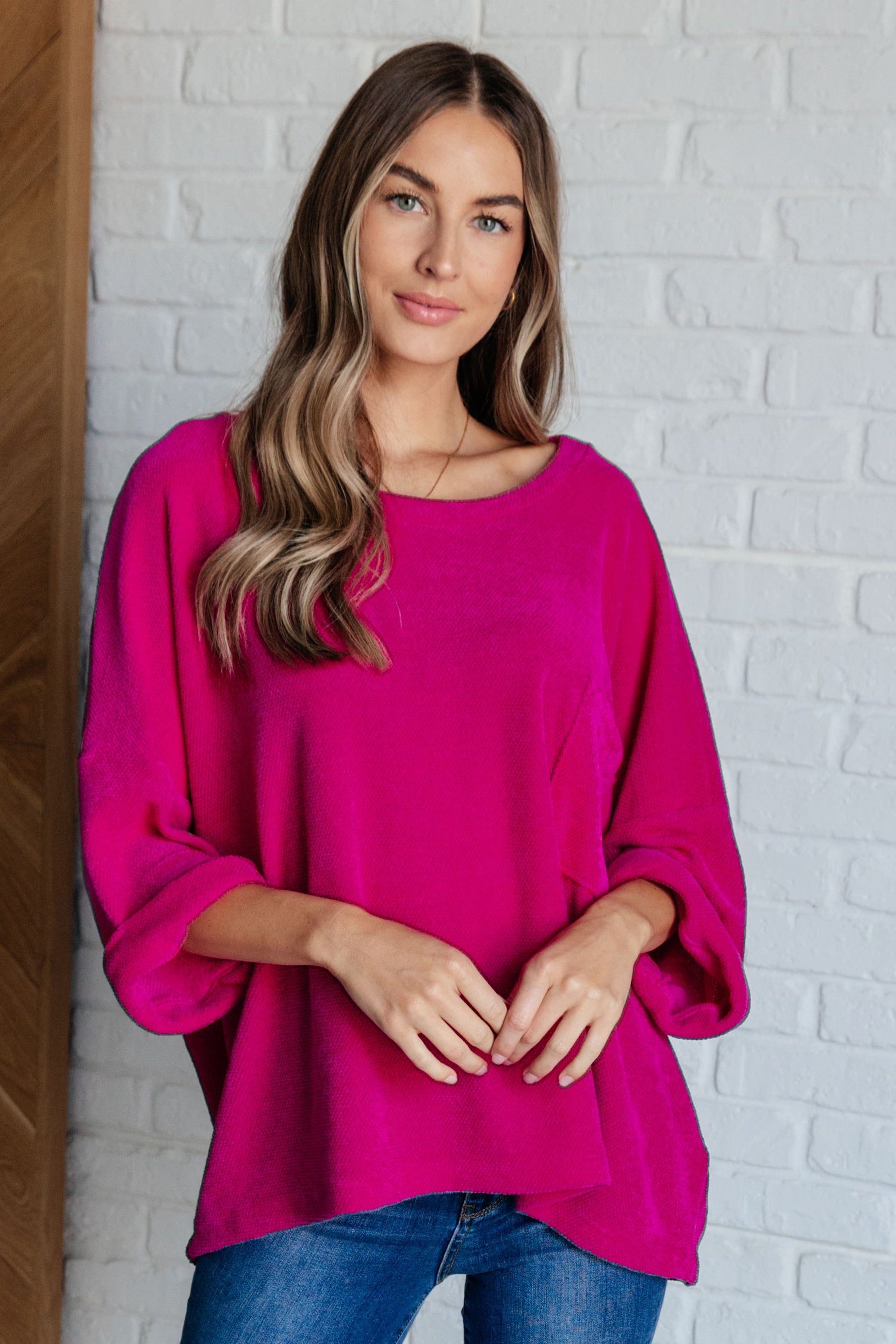 Woman wearing fuchsia chenille blouse with relaxed fit and rolled sleeves standing against white brick wall in eclectic style