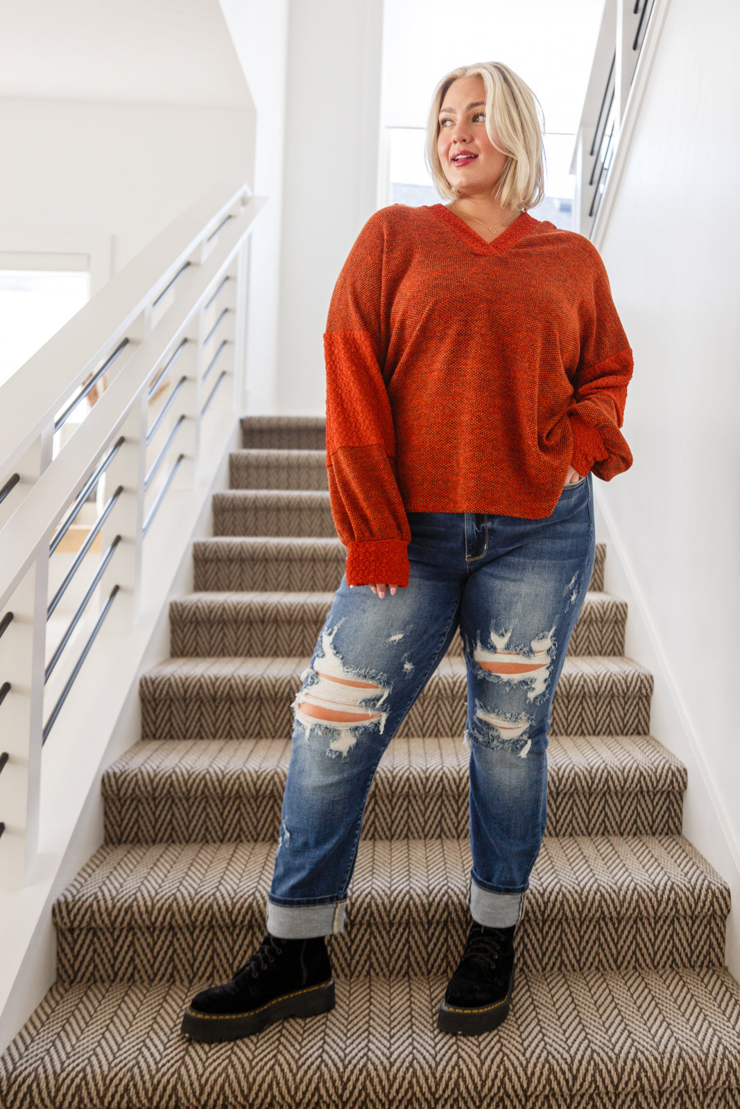 Woman wearing rust plush knit hoodie with voluminous sleeves paired with ripped rolled cuff denim jeans and black boots