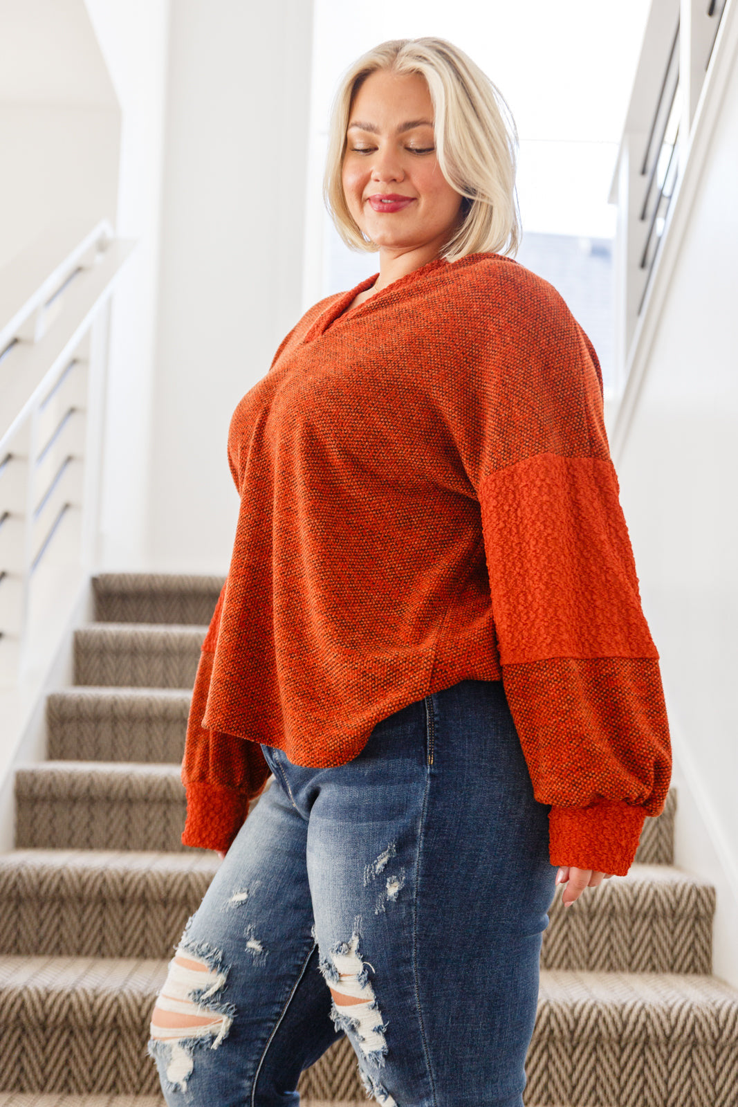 Woman wearing rust color block knit hoodie with textured sleeves paired with distressed denim jeans in eclectic style