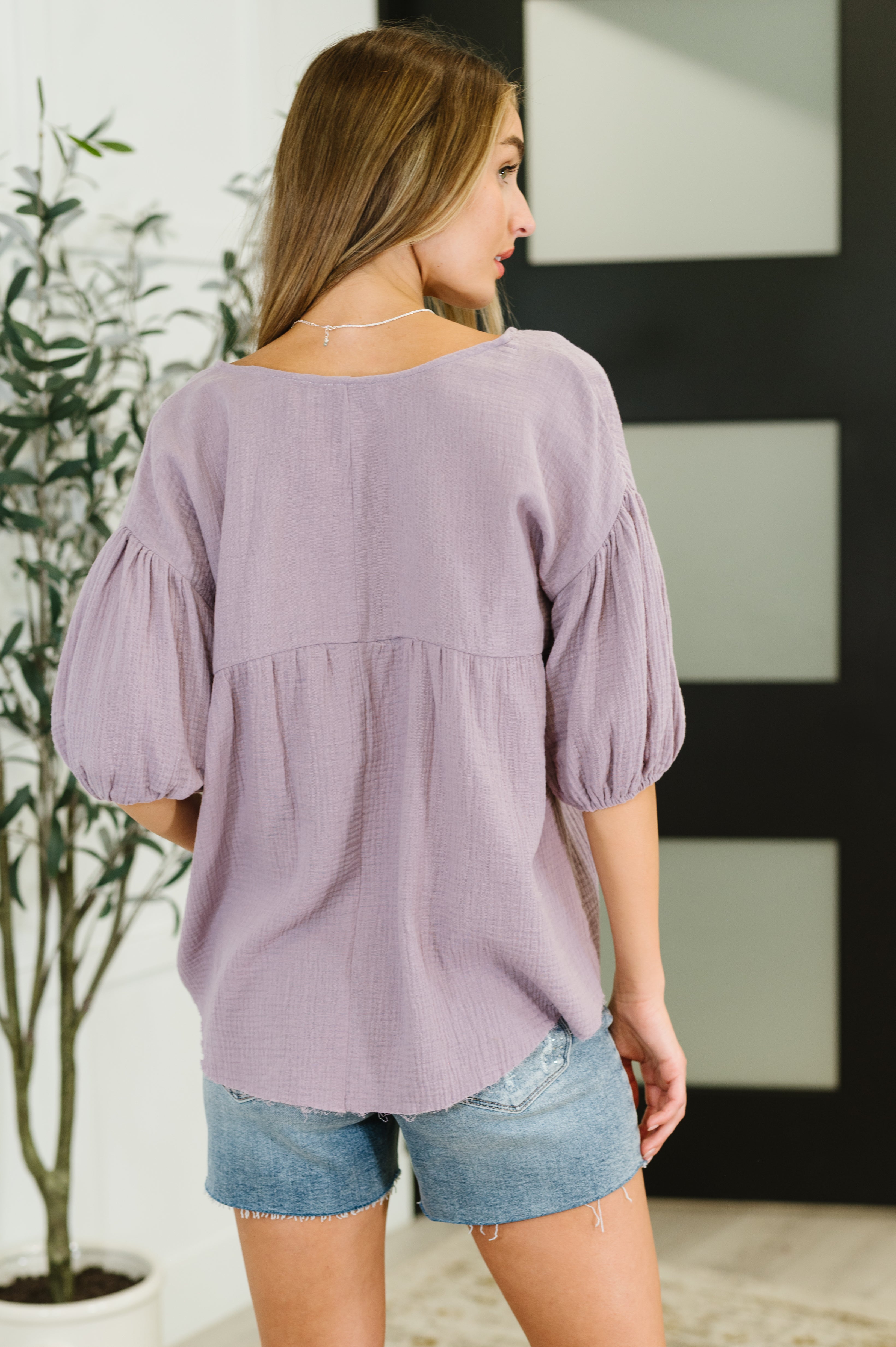 Woman wearing lavender bubble sleeve blouse with loose fit and textured fabric, styled casual and free-spirited from back view