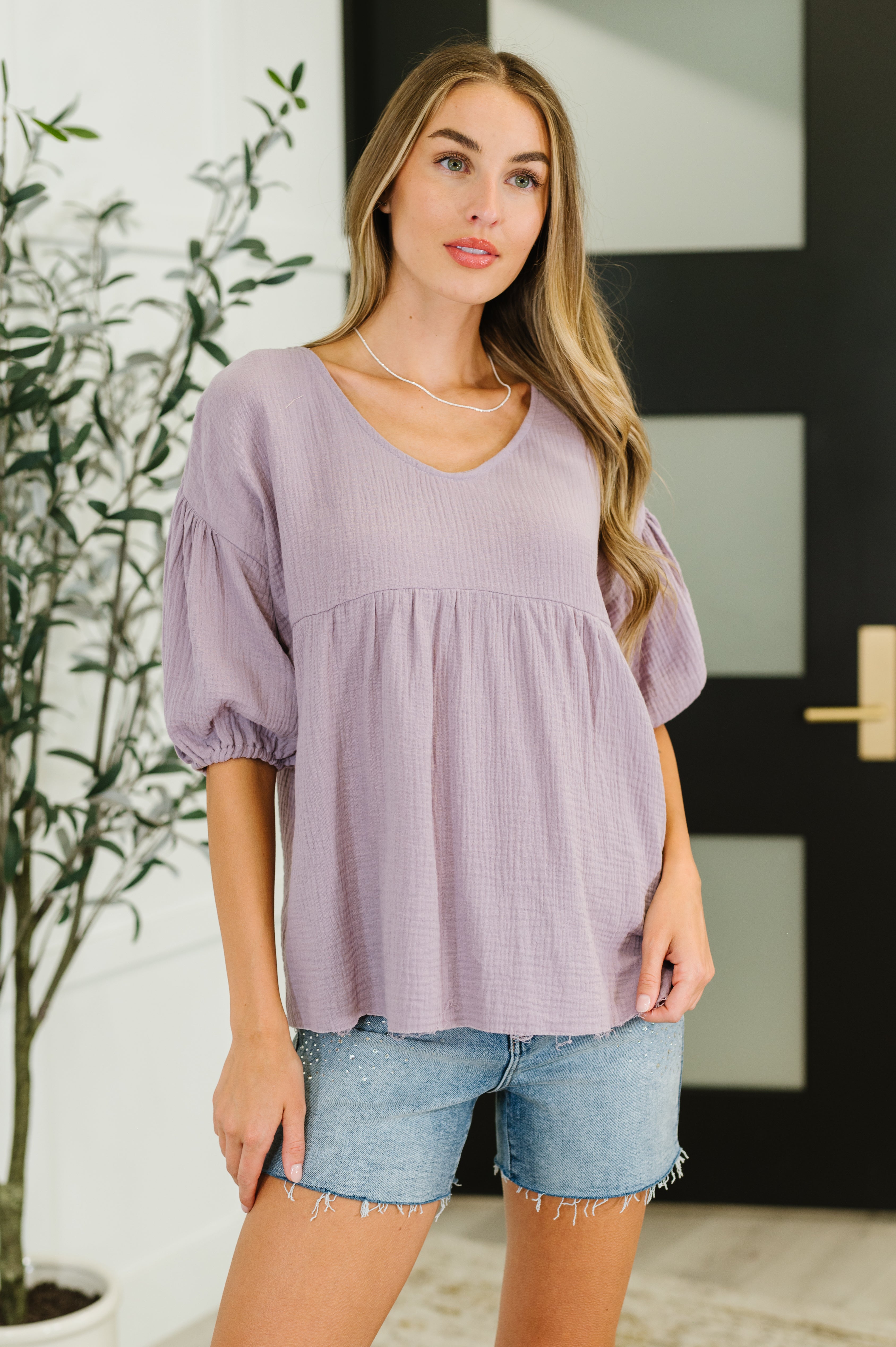 Woman wearing lavender peasant blouse with puff sleeves and loose fit paired with casual denim shorts in eclectic style