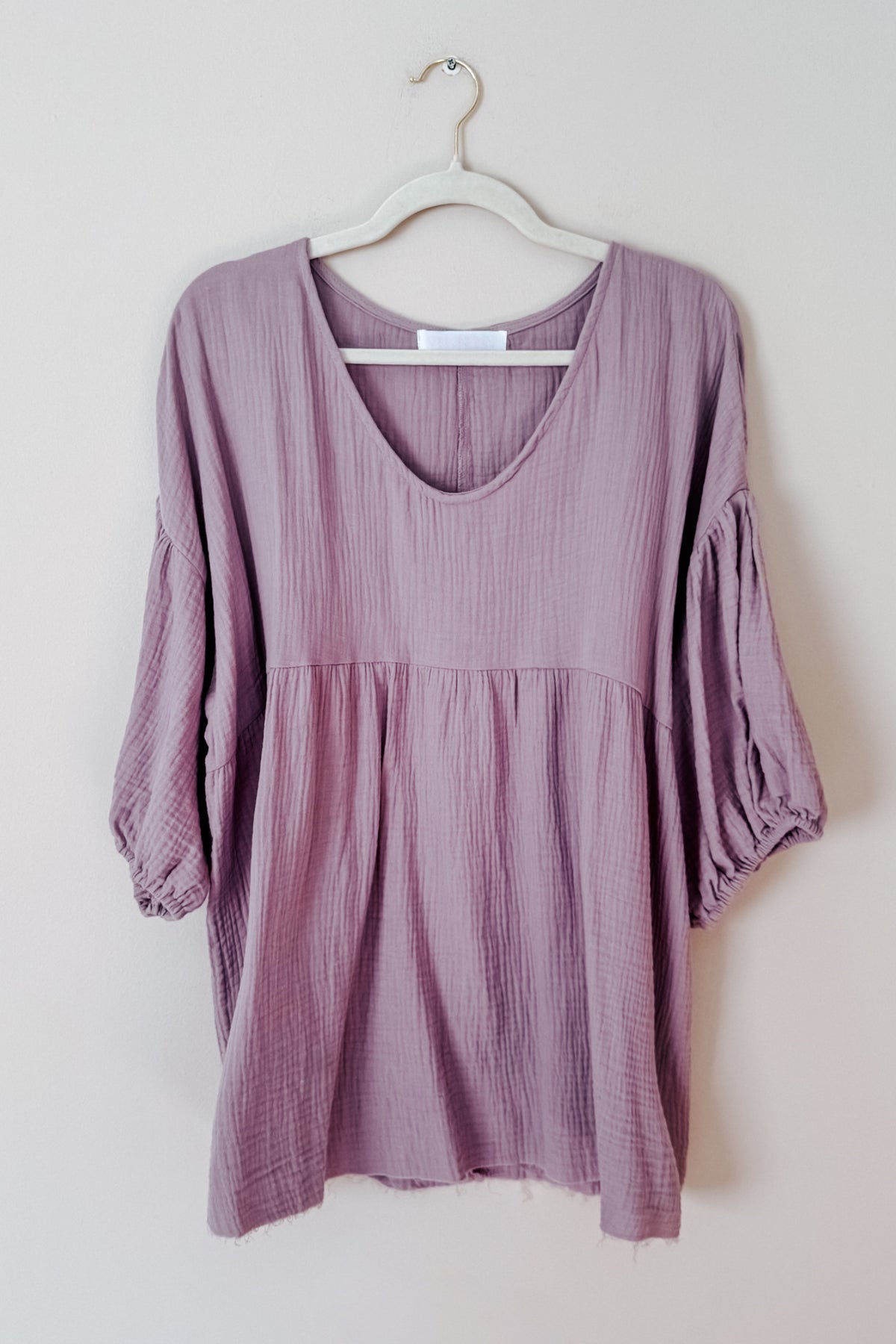 Purple cotton gauze peasant blouse with a soft V neck balloon sleeves babydoll silhouette and raw hem displayed on a hanger
