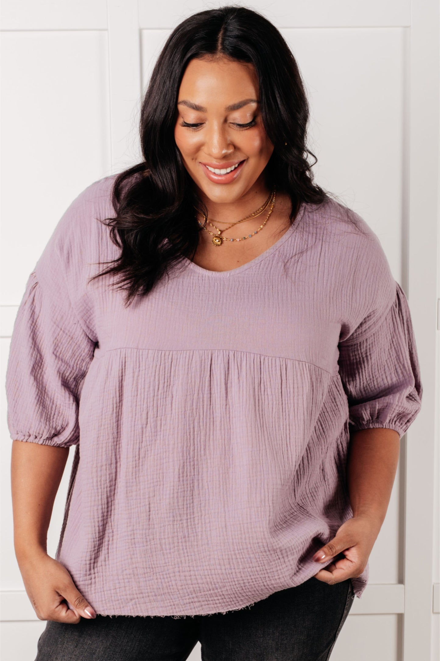 Woman wearing lavender bubble sleeve peasant blouse with textured fabric in relaxed, size-inclusive style smiling downwards