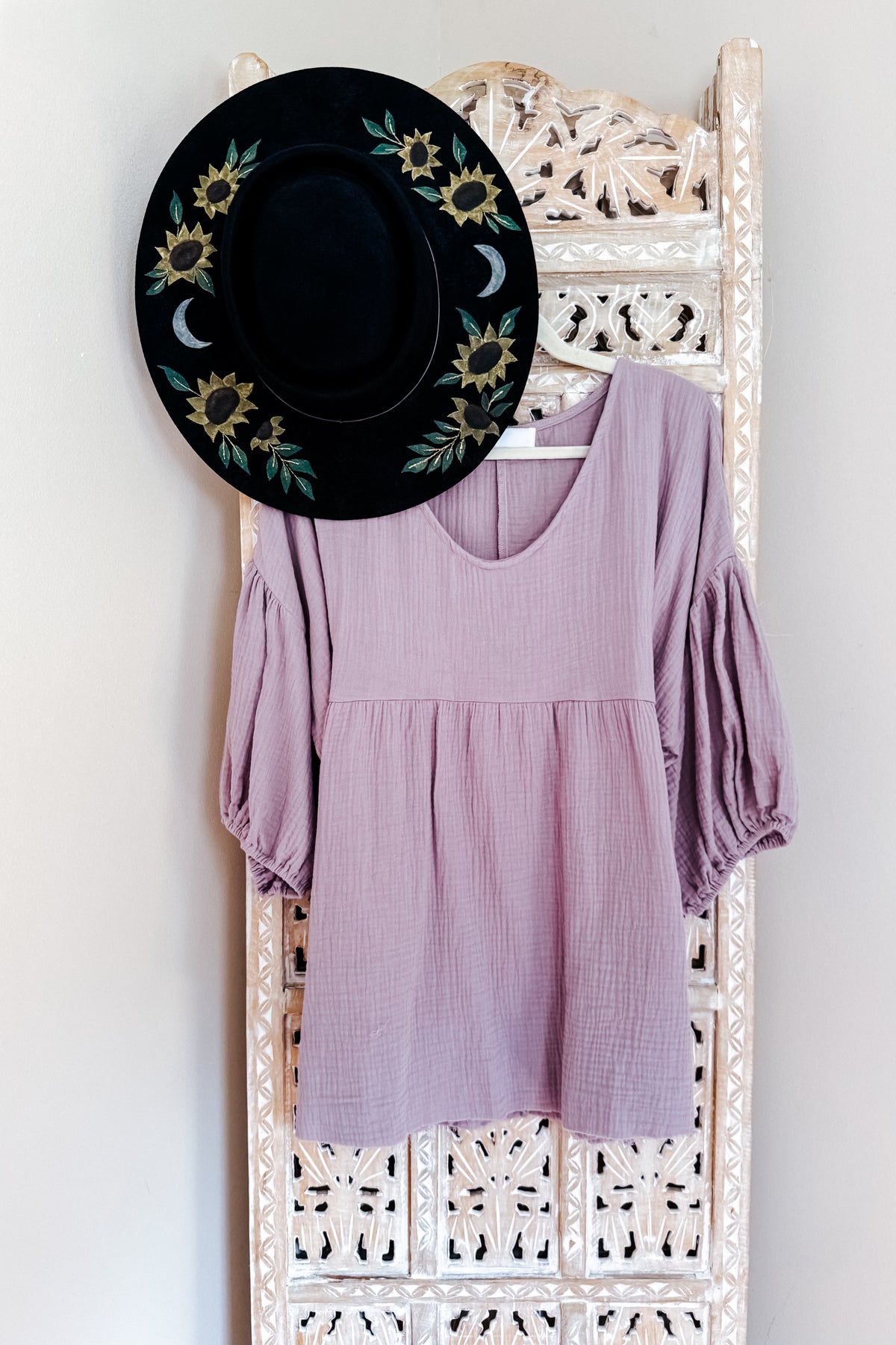 Purple cotton gauze peasant blouse with balloon sleeves soft V neck and babydoll shape displayed on an ornate white rack beneath a floral hat