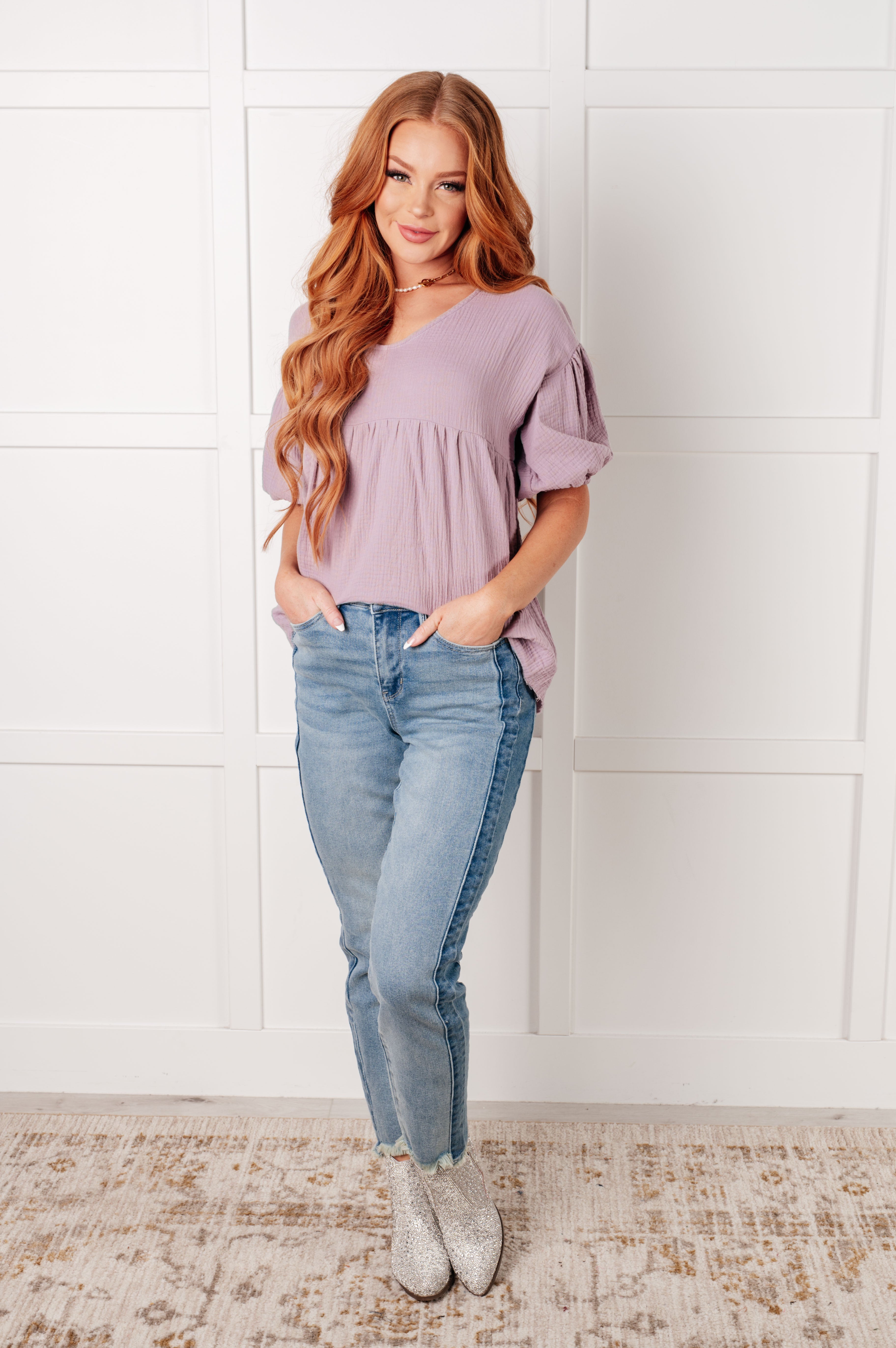 Woman wearing lavender bubble sleeve blouse in relaxed fit paired with light wash denim jeans and ankle boots