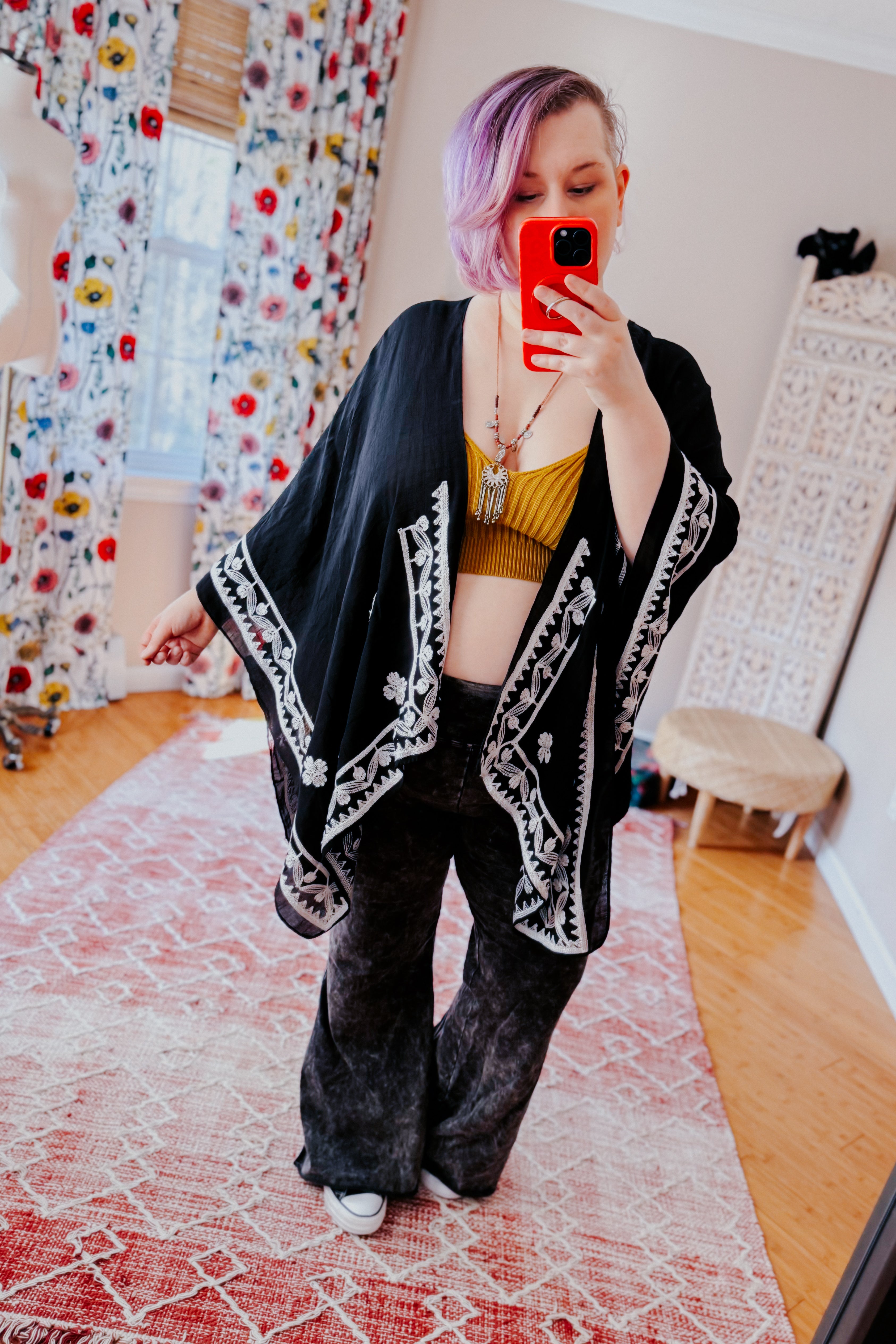 Woman wearing black layering piece with white floral embroidery over mustard crop top and loose dark pants in eclectic style