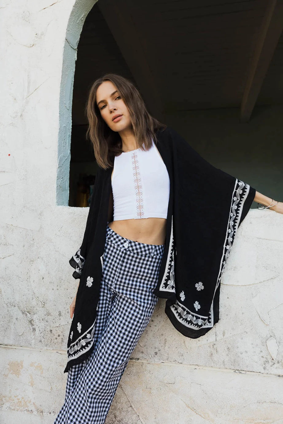 Woman wearing black embroidered layering piece with floral details paired with white crop top and checkered pants in bold style