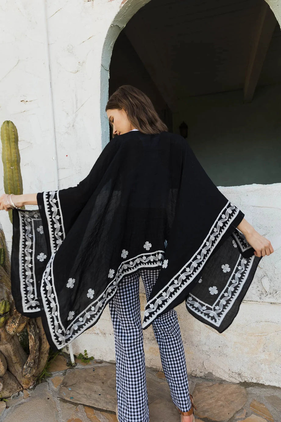 Woman showcasing black embroidered layering piece with white floral accents paired with gingham pants in eclectic style