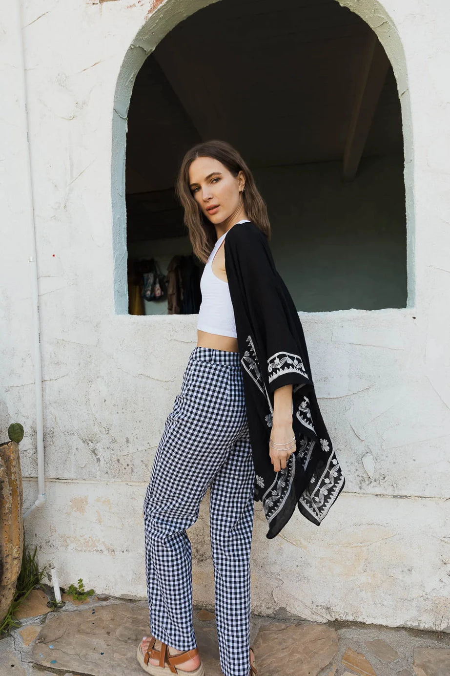 Woman styled in black embroidered layering piece with white floral patterns and gingham pants in eclectic, bold look