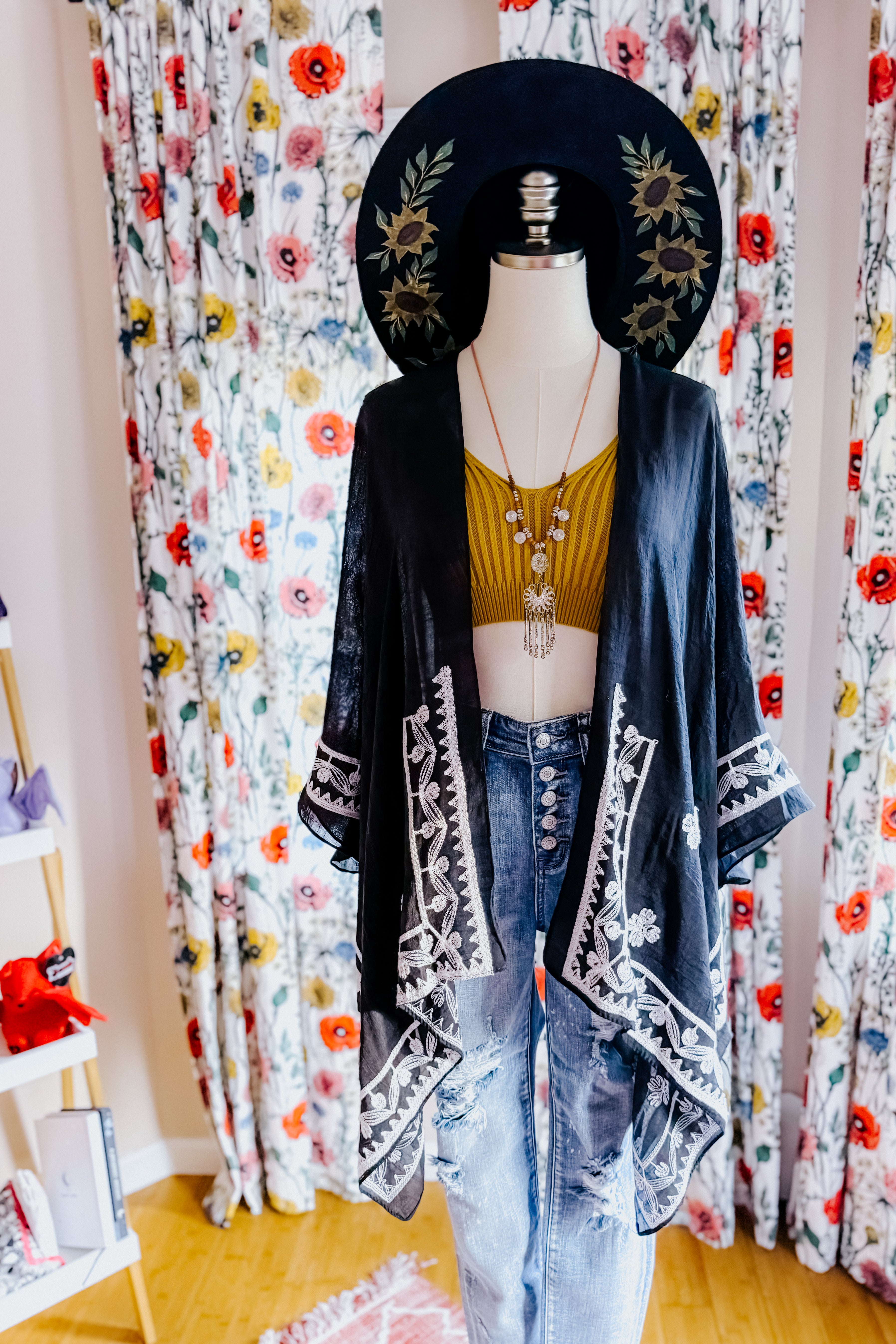 Mannequin wearing black layering piece with white embroidery over mustard crop top and high-waisted blue jeans in eclectic style