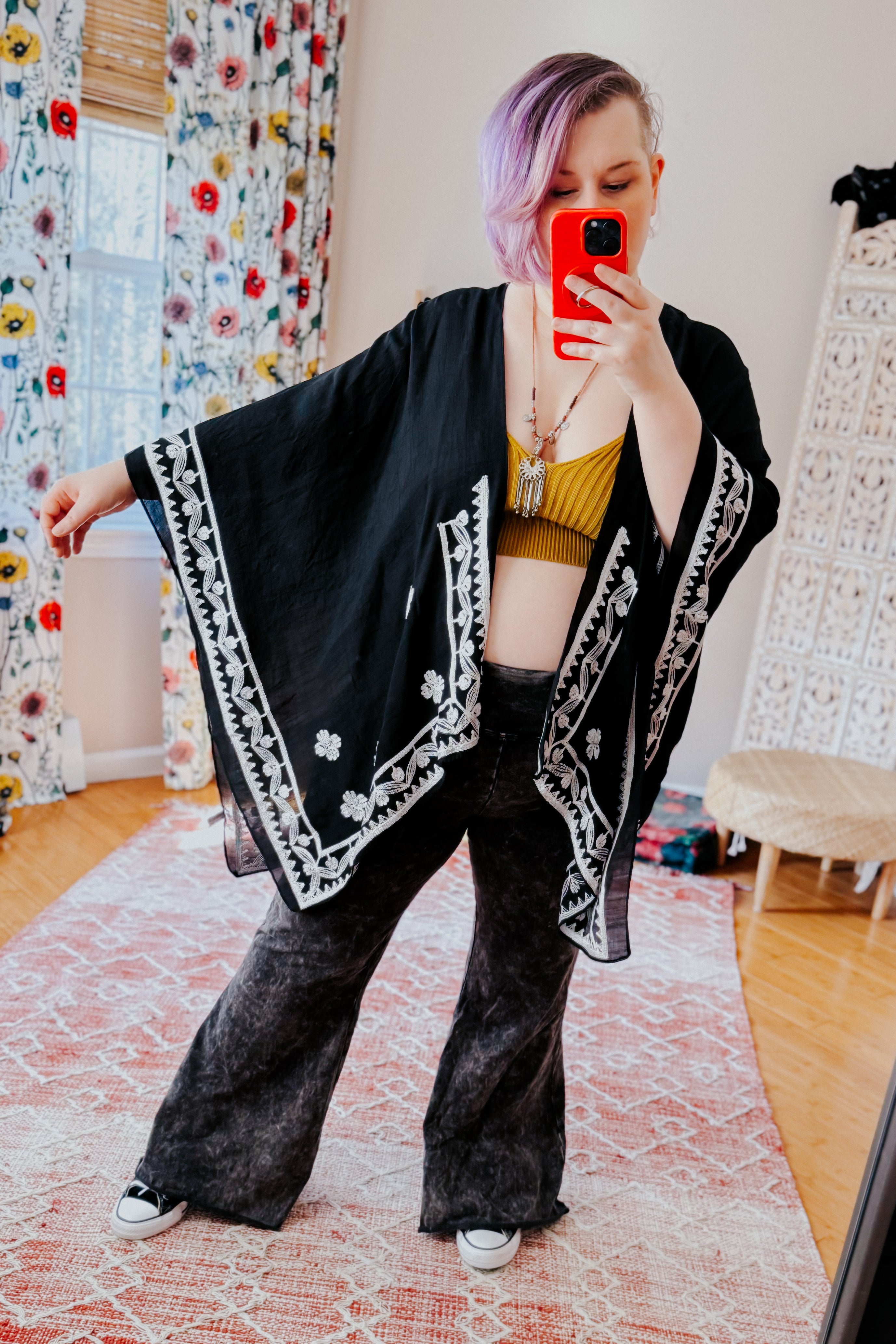 Woman wearing black embroidered layering piece with white floral borders over mustard top and wide-leg black pants in bold style