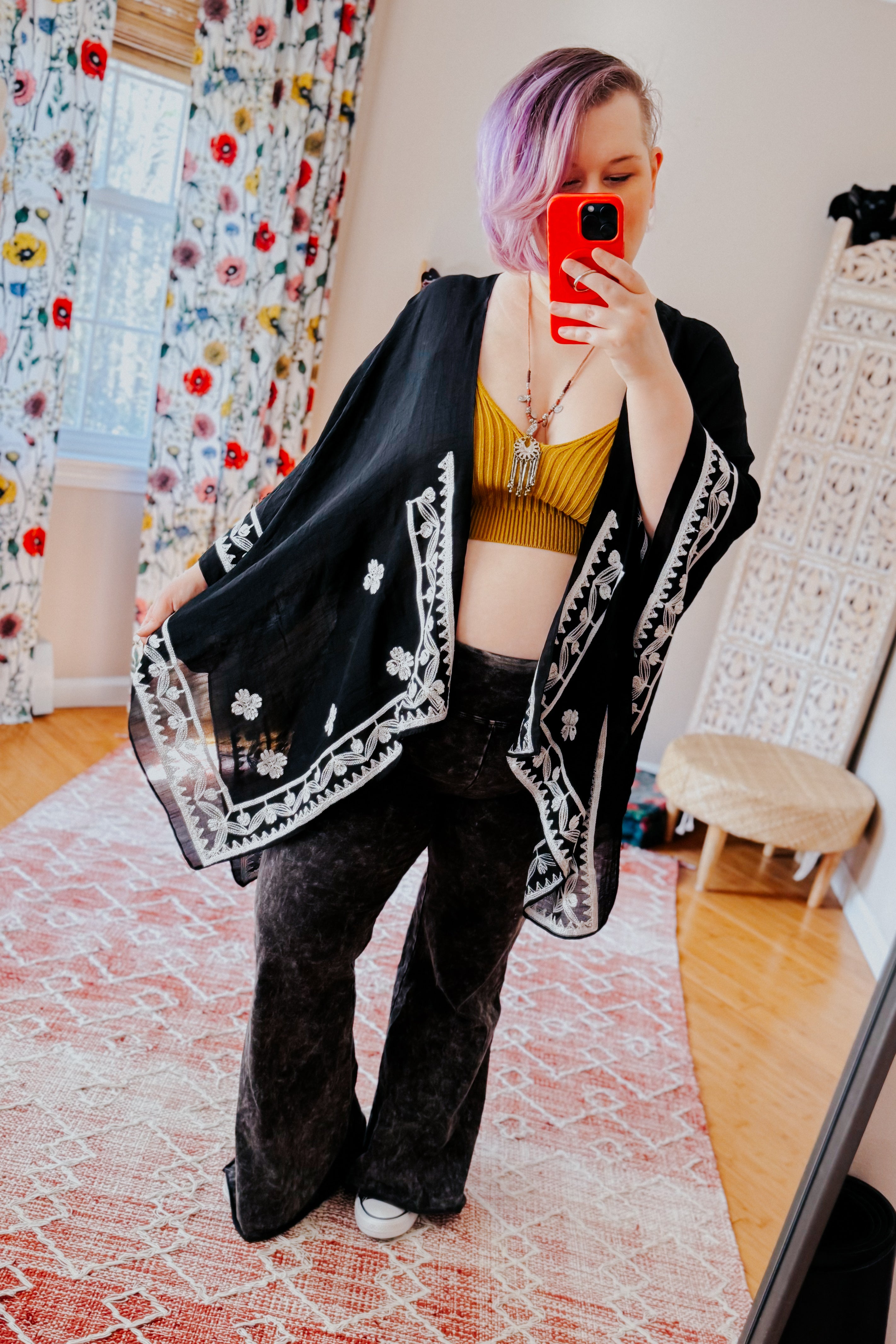 Woman wearing black embroidered layering piece with white floral designs over mustard ribbed crop top and wide-leg pants in eclectic style