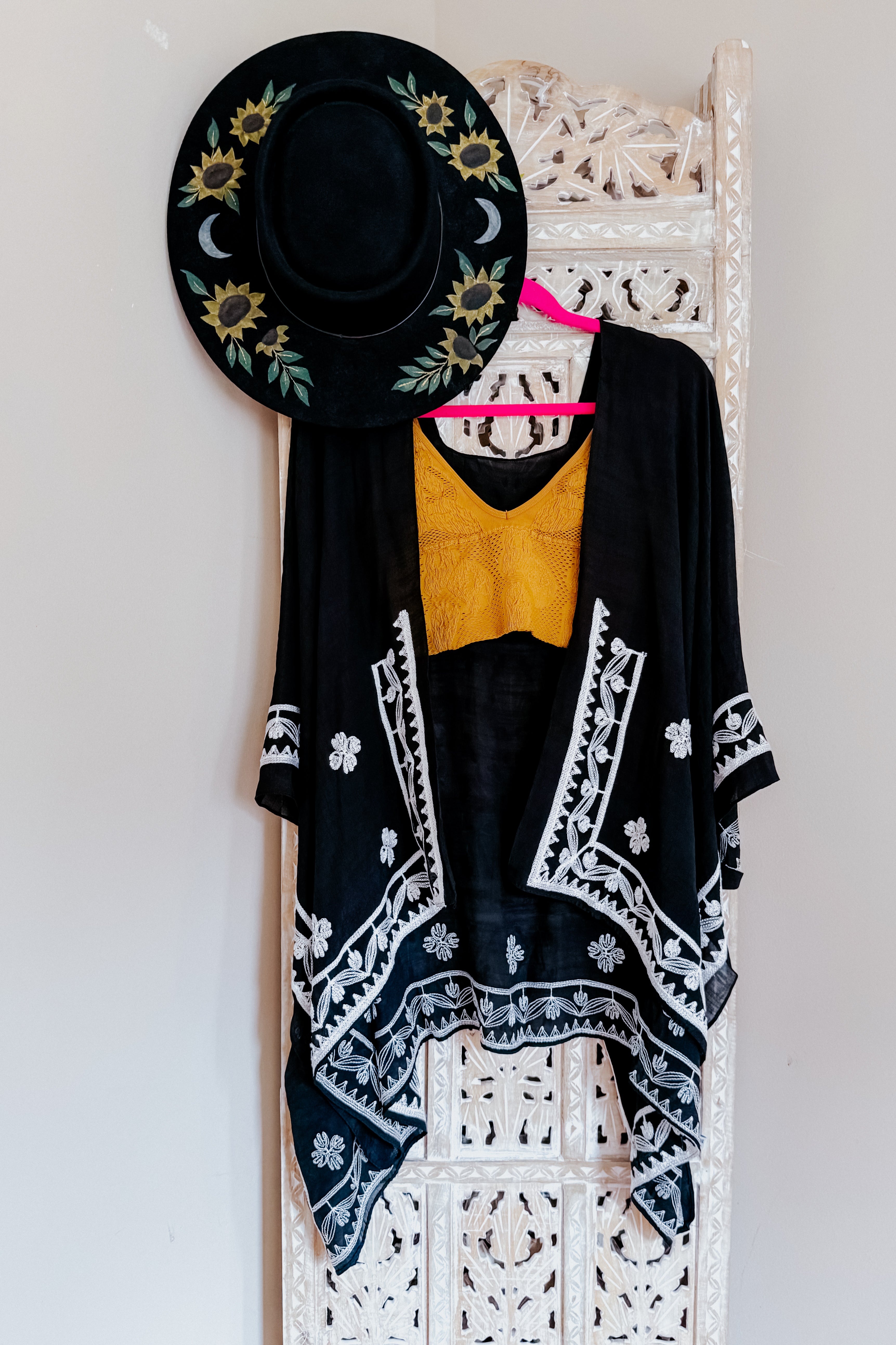 Black layering piece with white poppy embroidery paired with mustard textured top and sunflower-embroidered hat in eclectic style