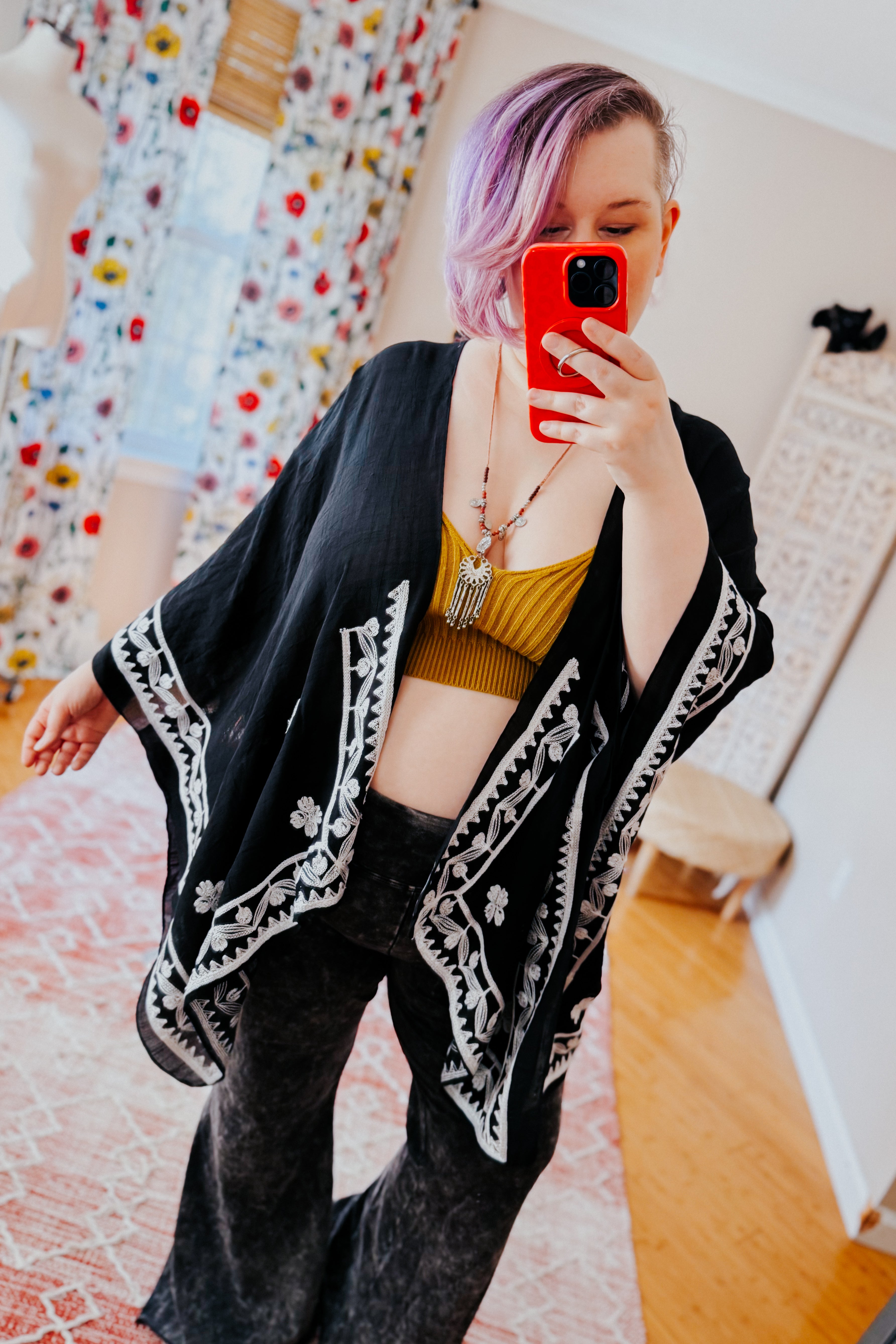 Woman wearing black layering piece with white poppy embroidery paired with mustard crop top and loose dark pants in eclectic style