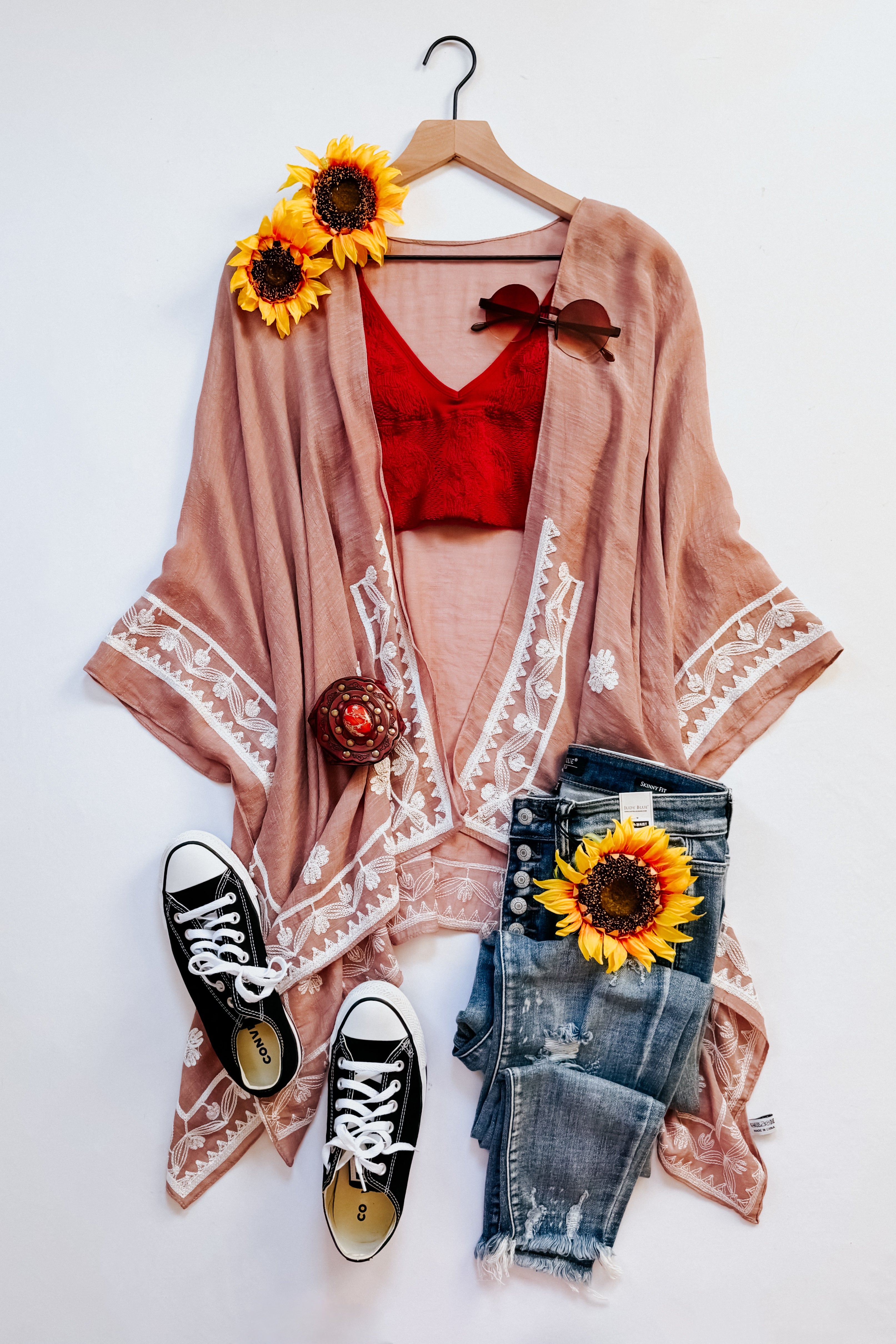Blush taupe embroidered draped layering piece paired with red crop top, distressed jeans, black sneakers, and sunflower accents in eclectic style