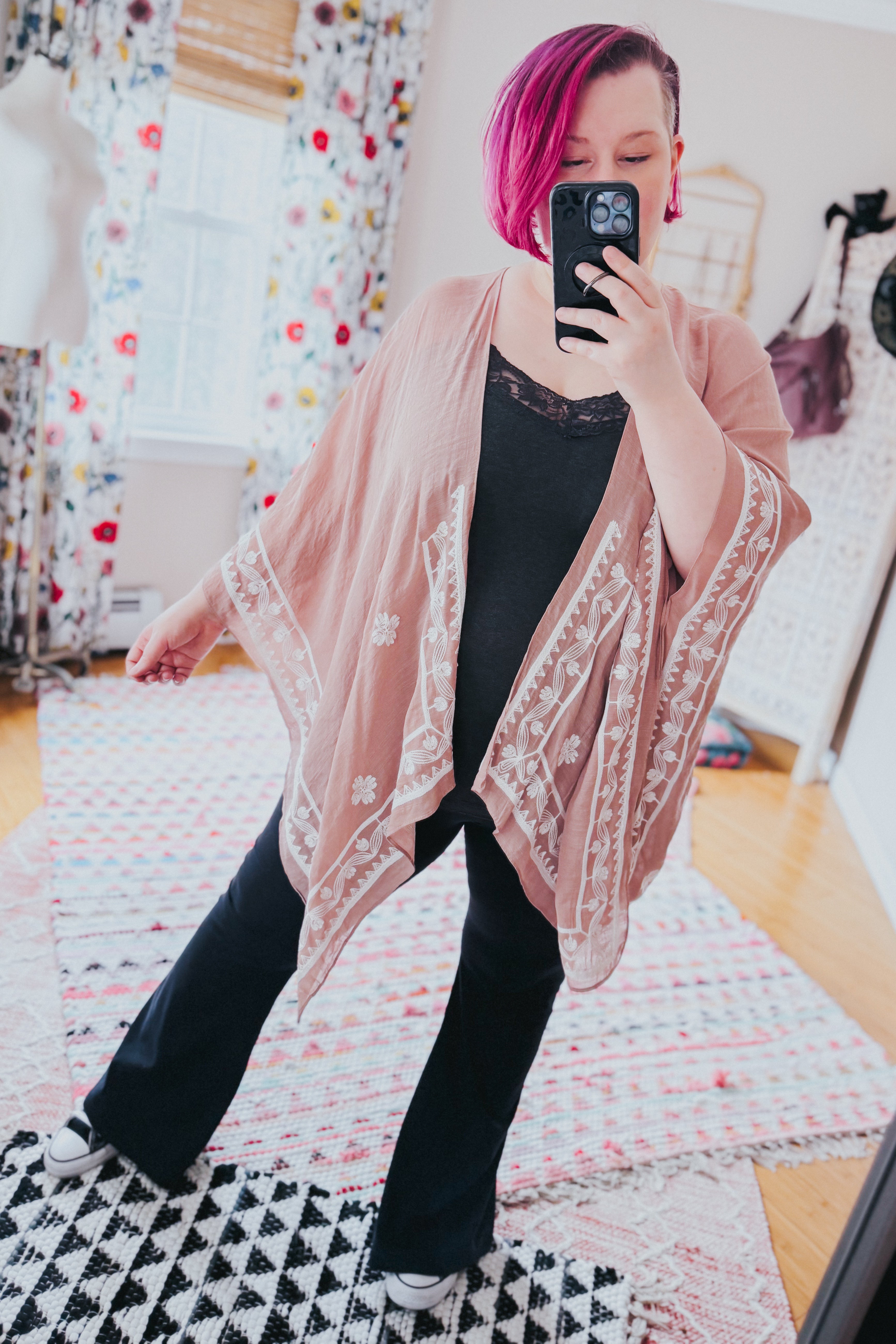 Woman with vibrant magenta hair modeling blush taupe layering piece with white poppy embroidery over black outfit indoors