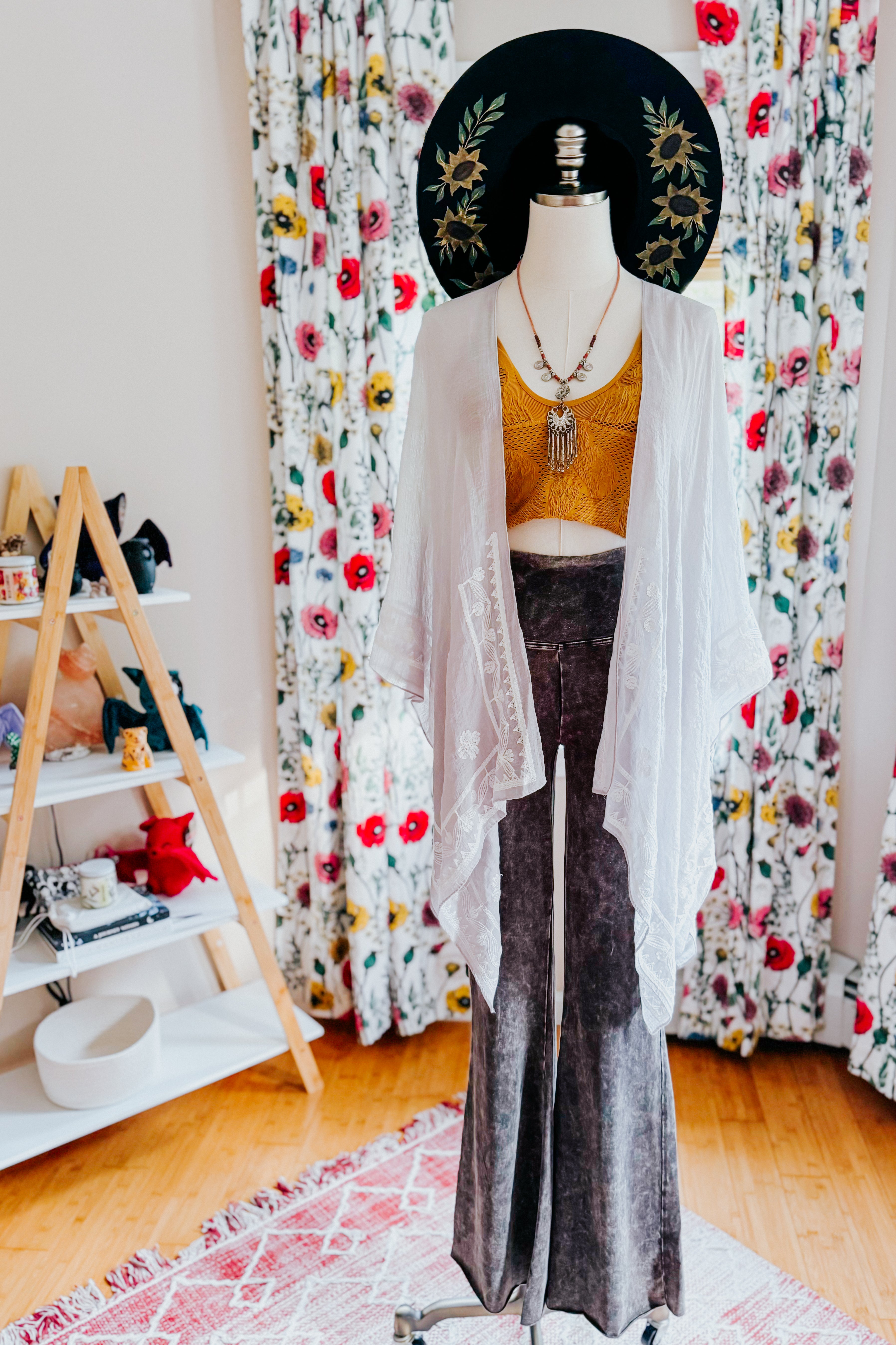 Mannequin dressed in stone layering piece with floral embroidery over mustard top and textured wide-leg pants indoors