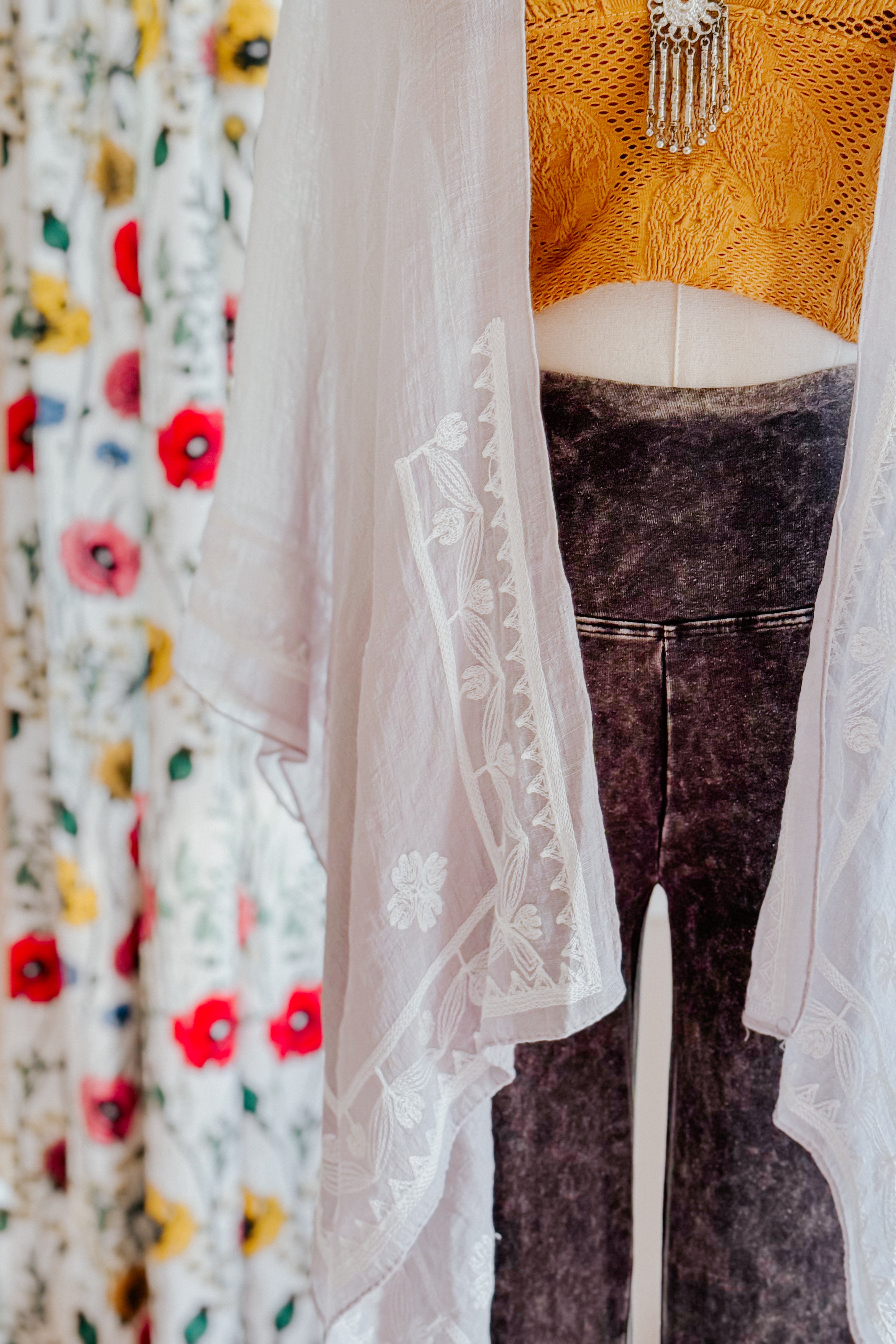 Sheer stone layering piece with delicate poppy embroidery draped over mustard knit top and charcoal leggings on mannequin