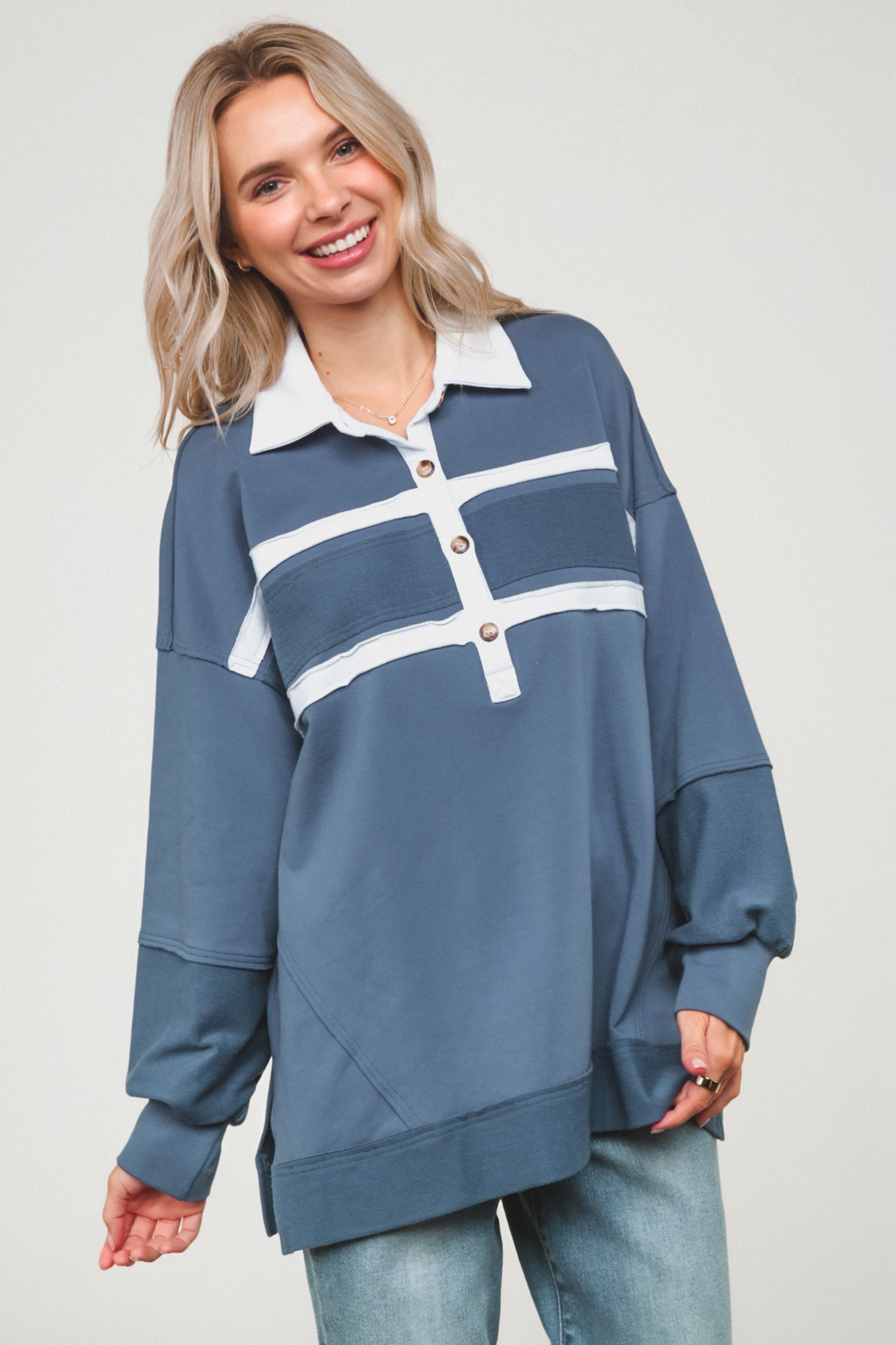Smiling woman wearing oversized steel blue polo top with white collar and horizontal stripe details paired with jeans