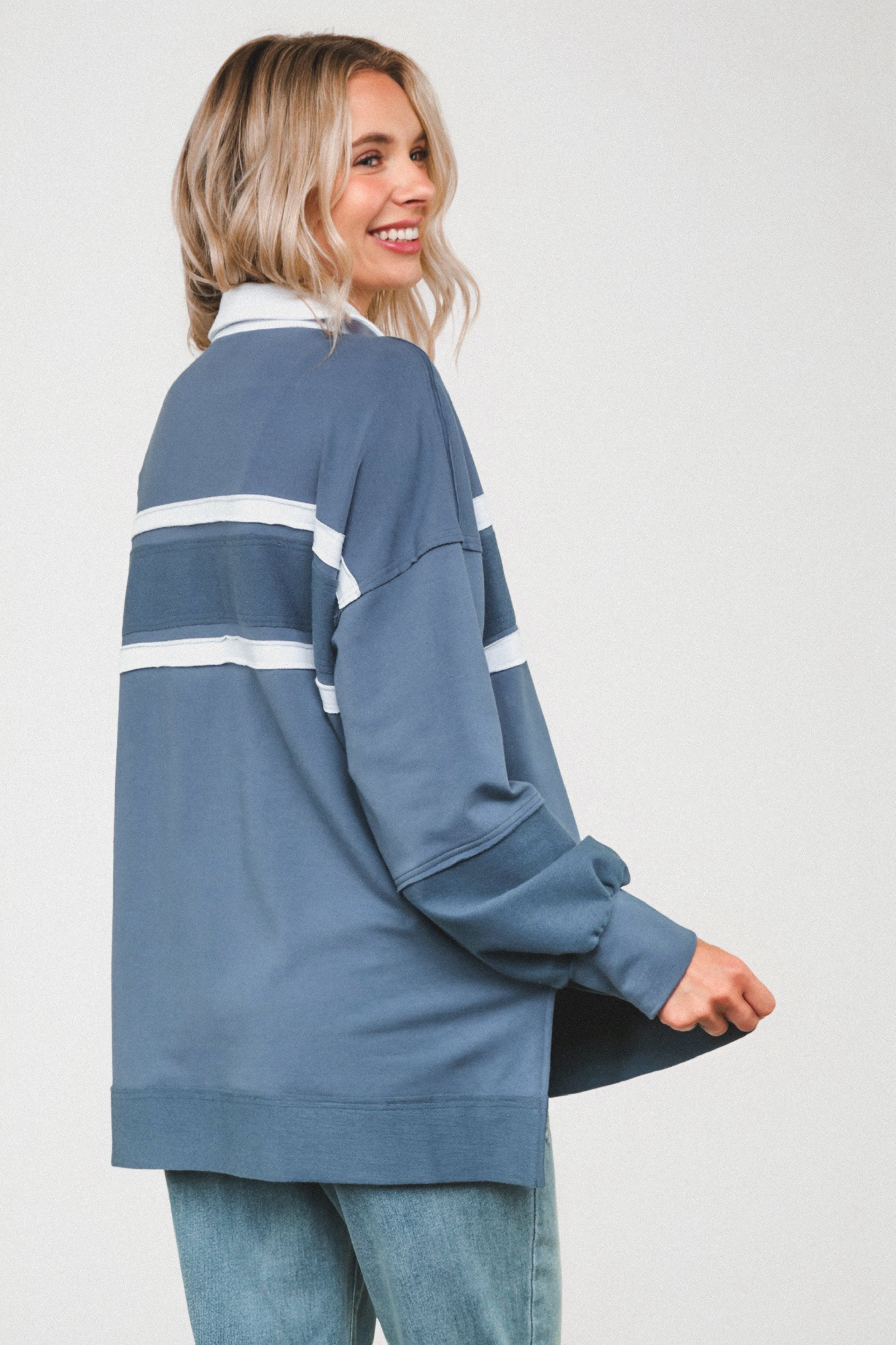 Smiling woman wearing slate blue casual top with white horizontal stripes and cuffed sleeves against plain background
