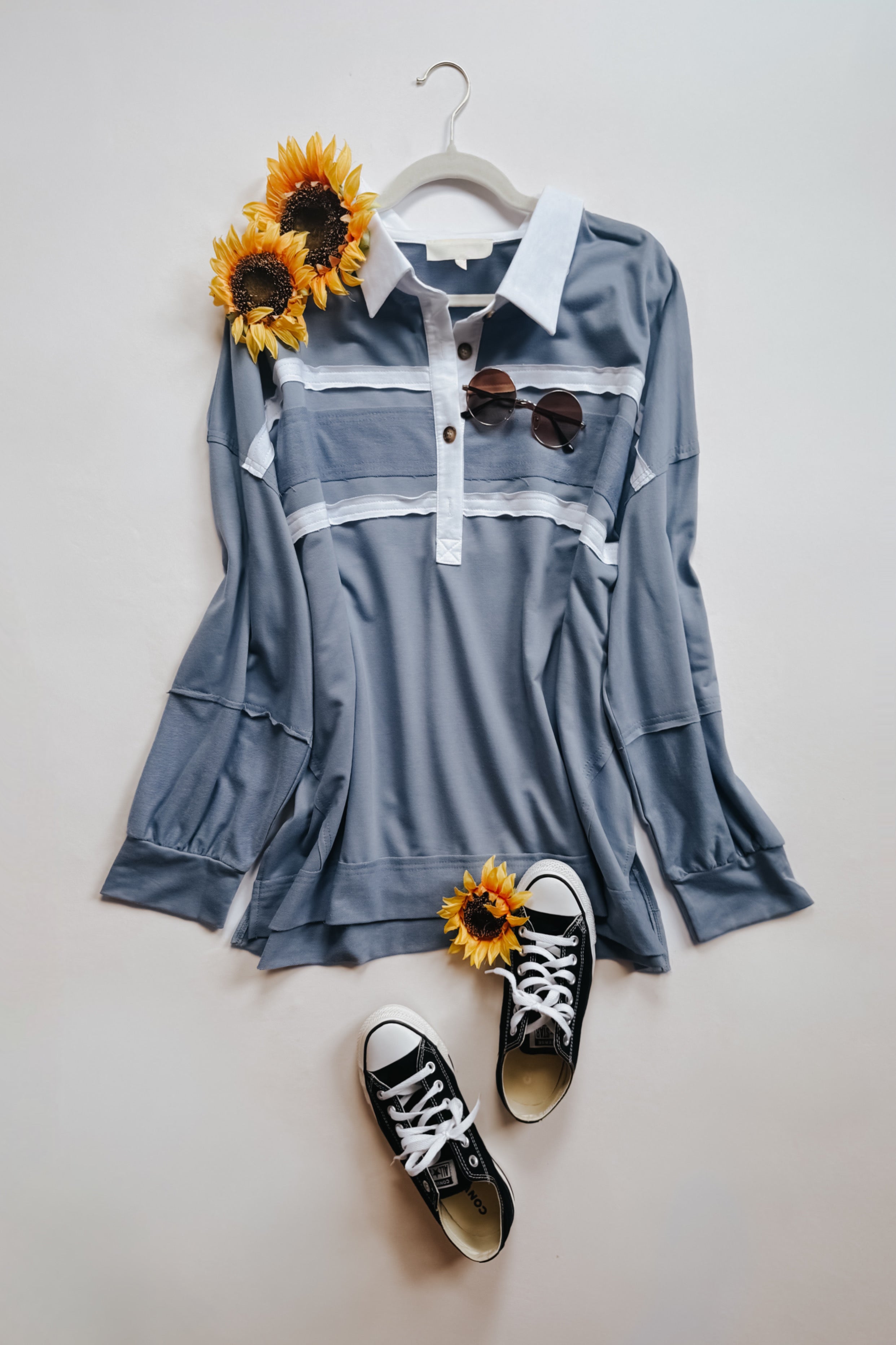 Slate blue long-sleeve polo with white collar and horizontal stripes paired with black canvas sneakers and sunglasses