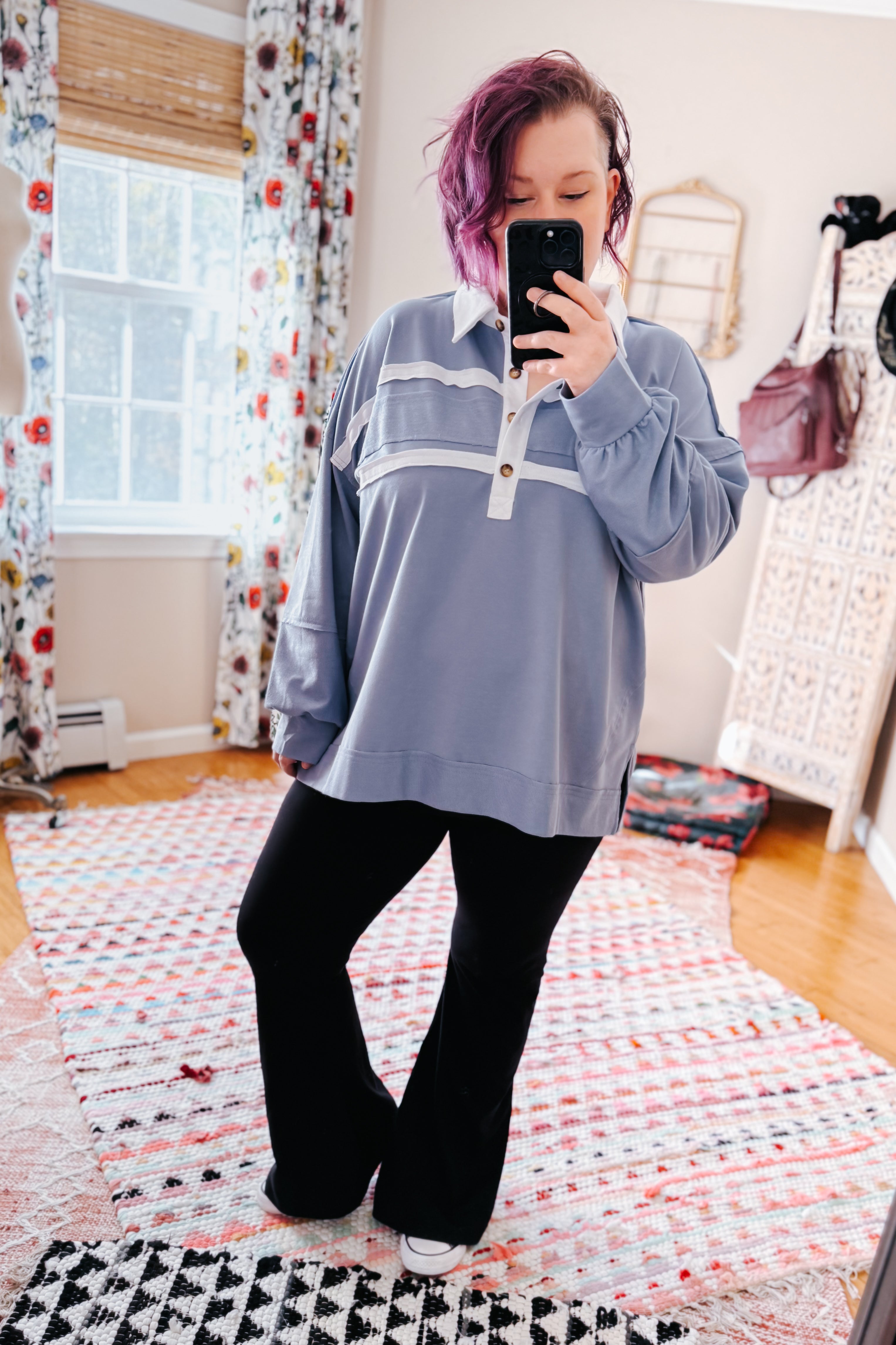 Woman with purple hair wearing relaxed steel blue polo top with white collar and stripes paired with black flared pants taking mirror selfie