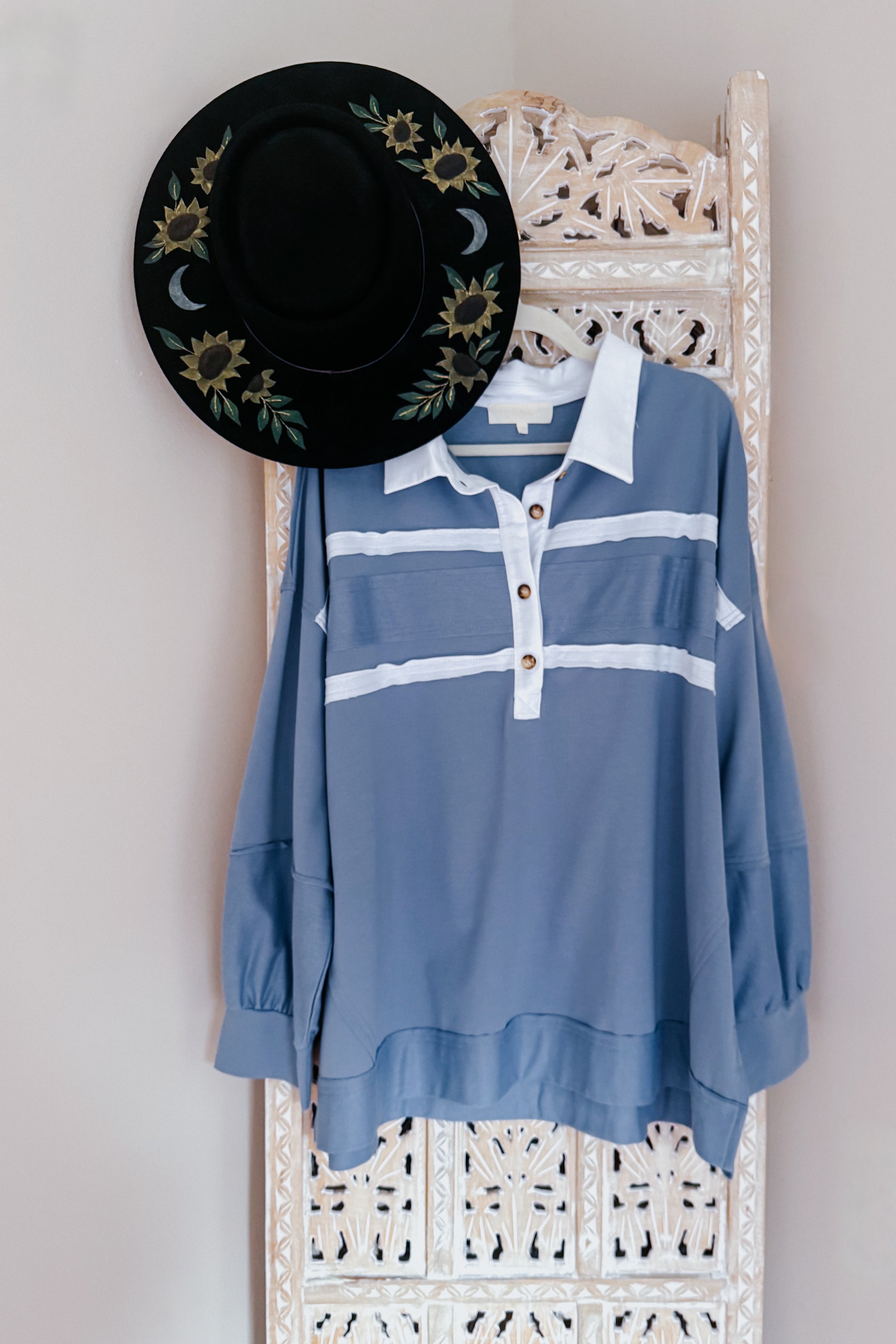 Slate blue polo top with white stripes and wooden buttons hanging on carved wooden screen with black embroidered hat