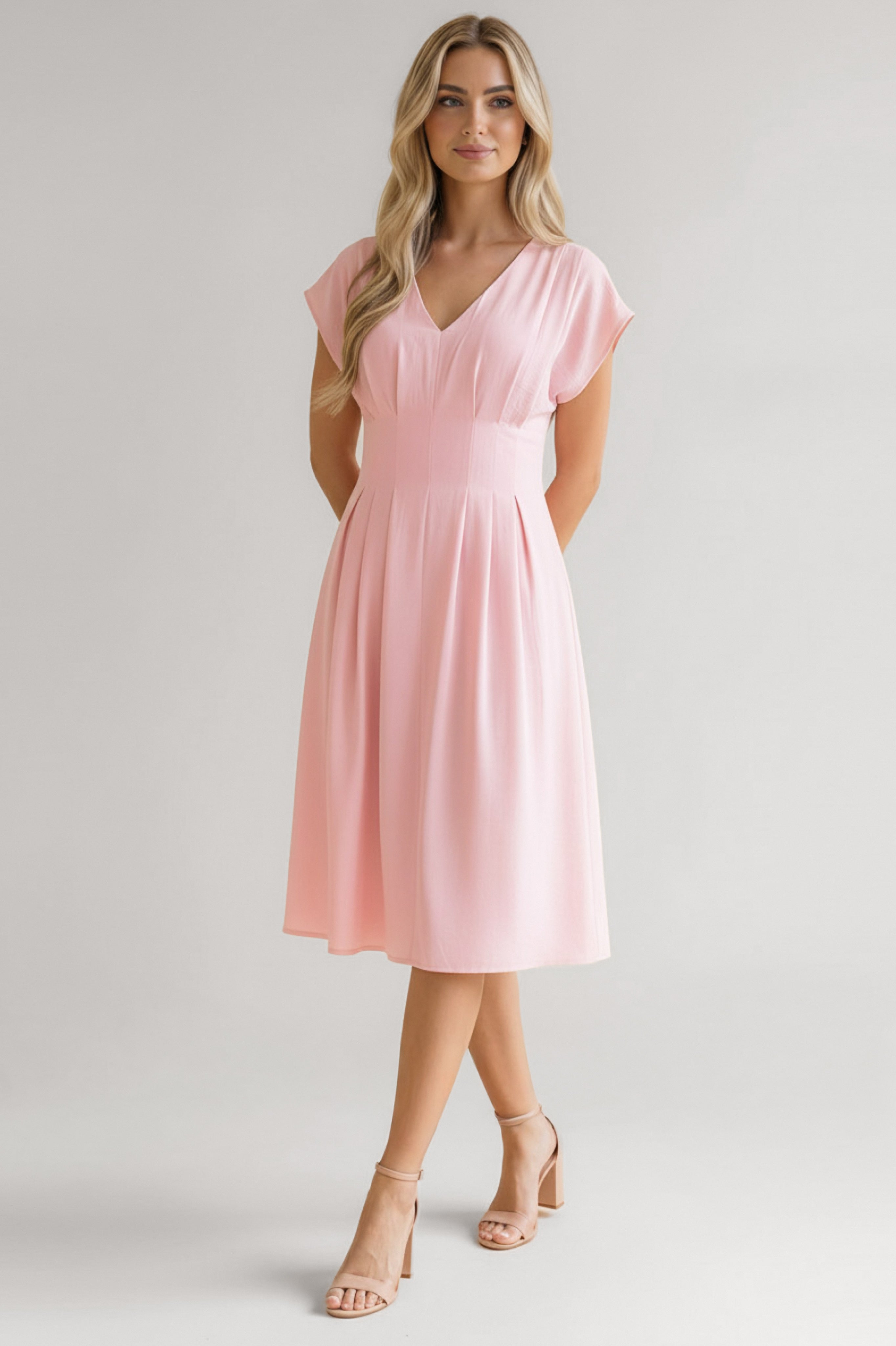 Woman in a pink midi dress with a V-neck, short sleeves, fitted waist, and pleated skirt paired with nude heels