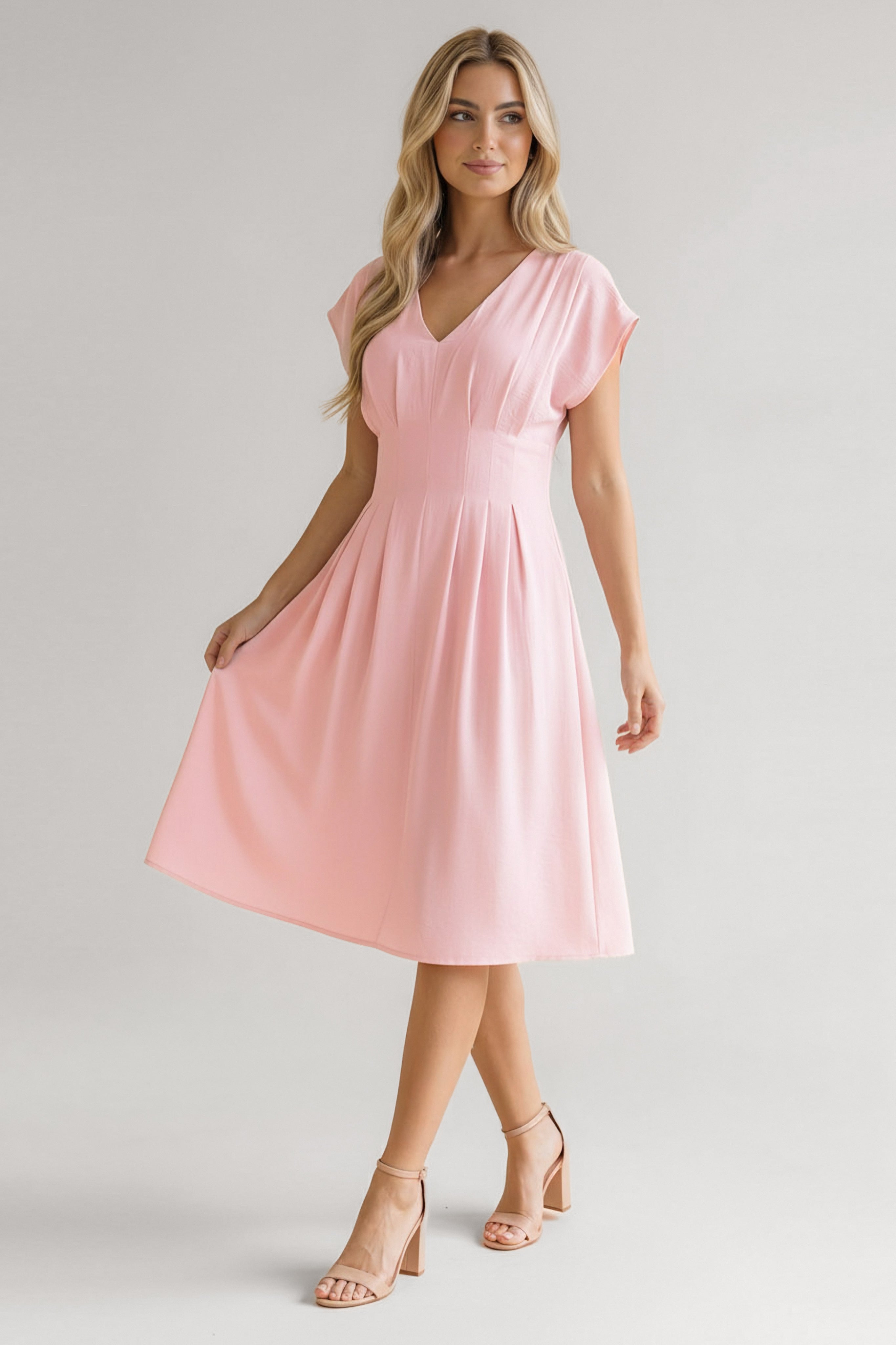 Woman wearing a soft pink dress with a V-neck, cap sleeves, fitted waist, and flowing midi skirt paired with nude heels