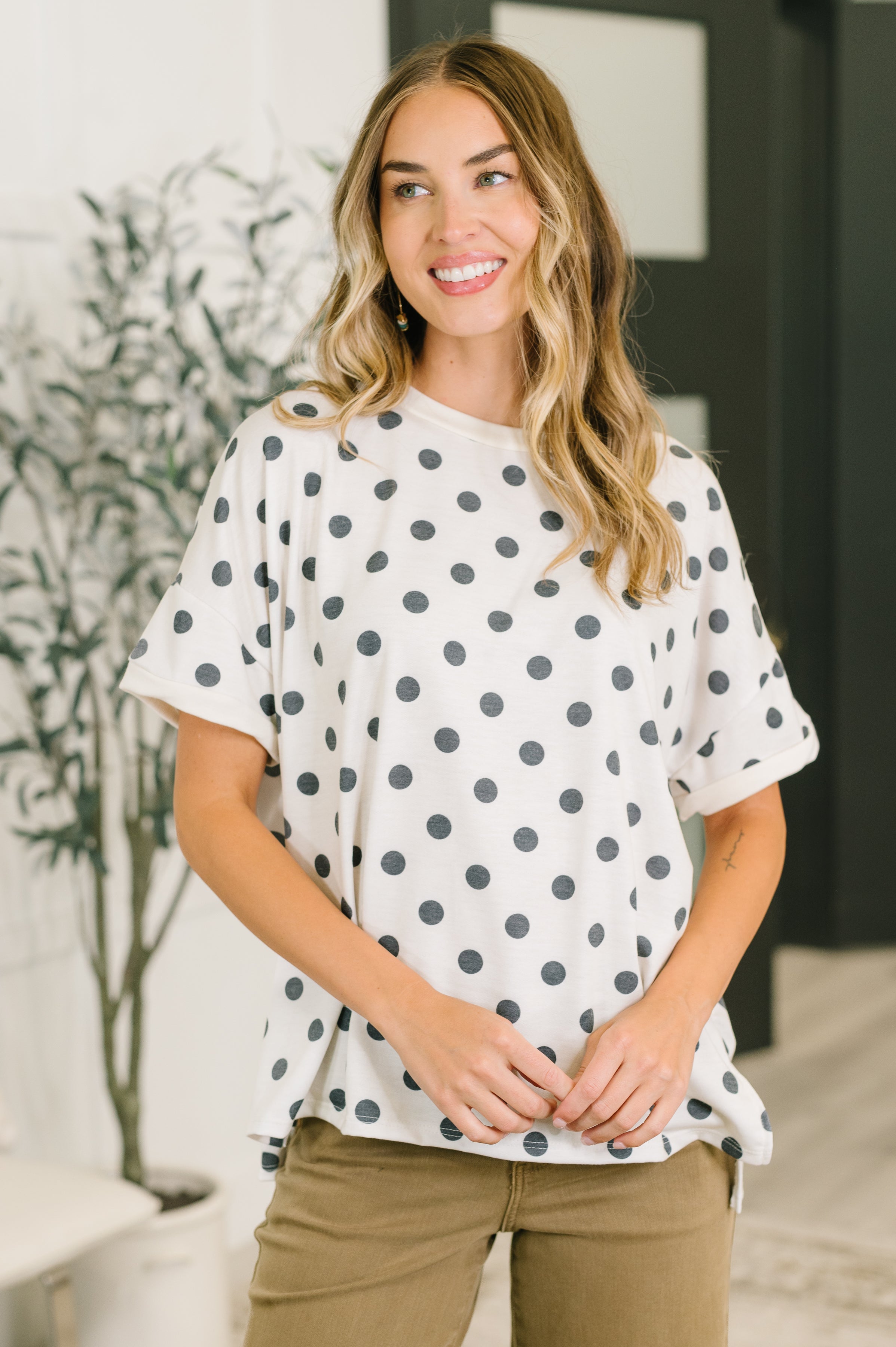 Woman smiling indoors wearing ivory oversized tee with black polka dots and olive pants with relaxed fit
