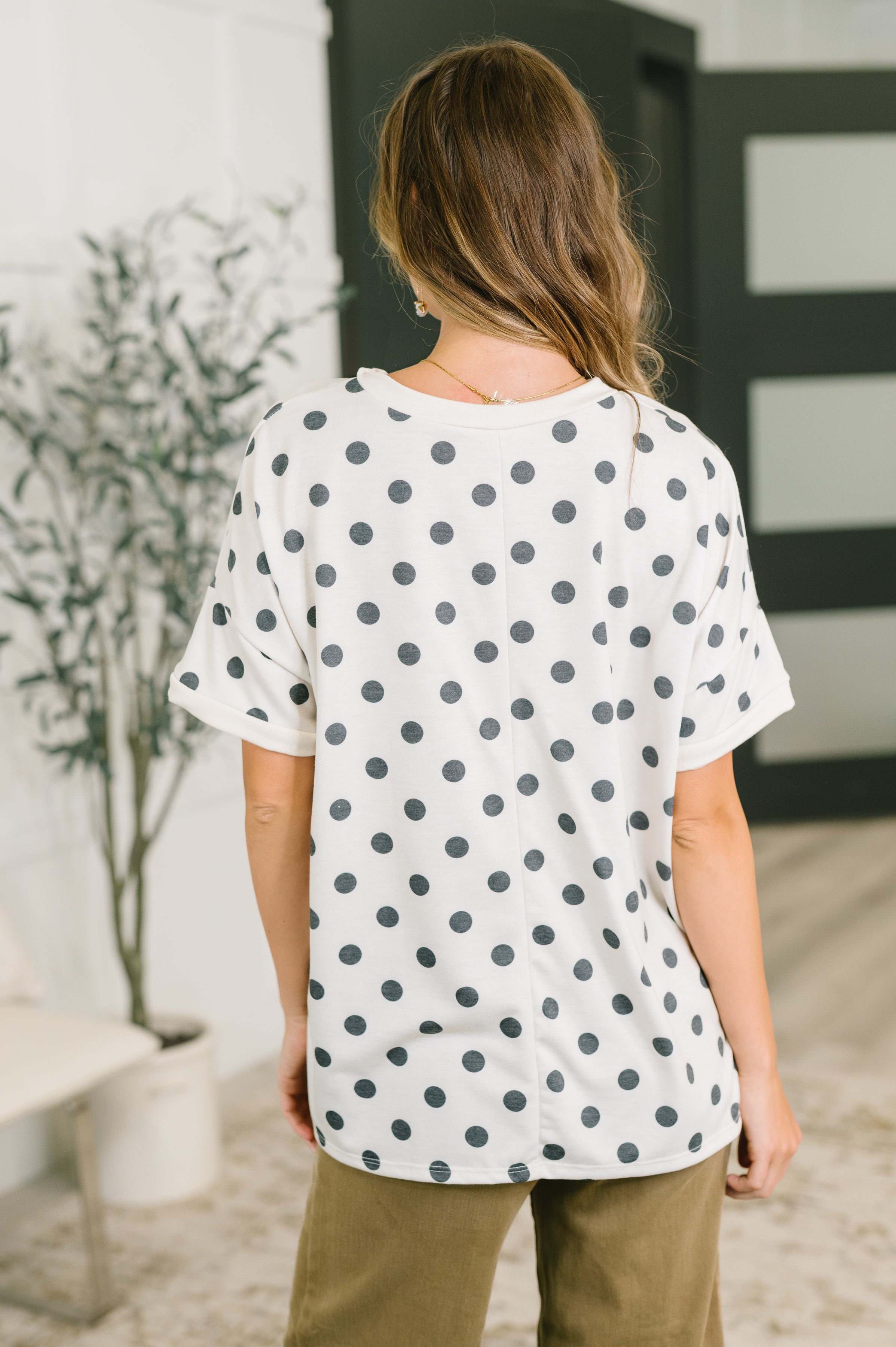 Woman seen from behind wearing ivory oversized tee with black polka dots and olive pants indoors