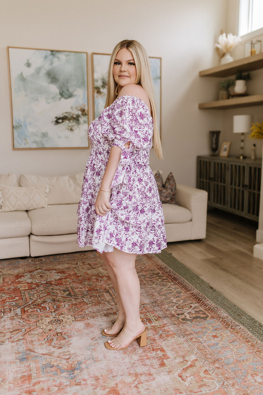 Plus size woman in free-spirited purple floral dress with puff sleeves and off-shoulder style in eclectic living room