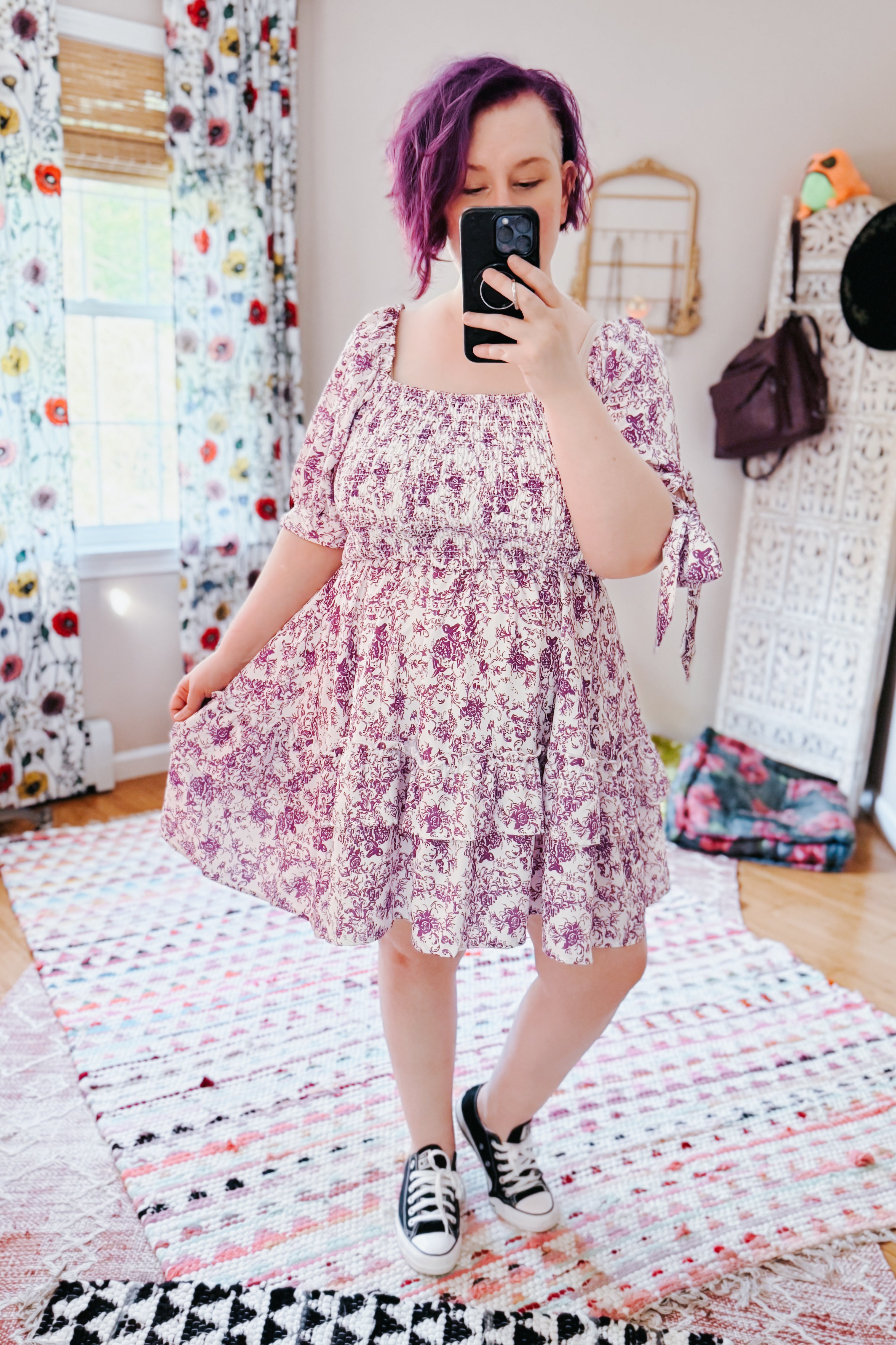 Woman with purple hair in a purple floral summer dress with puff sleeves and sneakers in a bright eclectic room