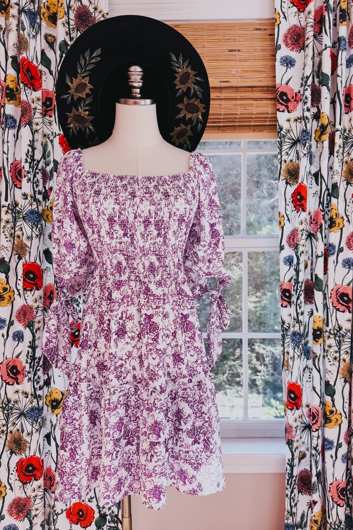 Purple floral babydoll dress with a smocked square neckline long sleeves and ruffled tiered skirt displayed on a mannequin